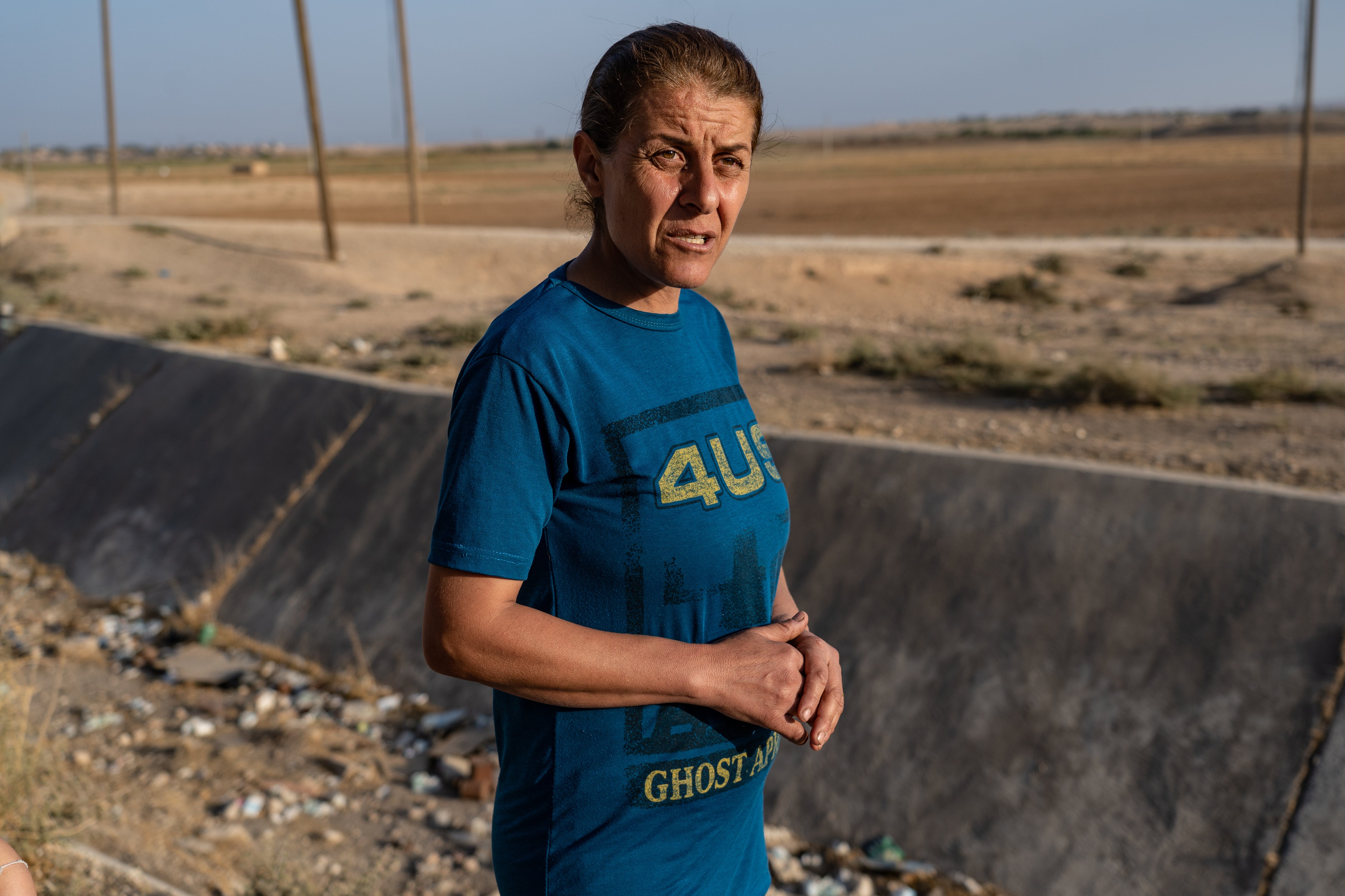An Assyrian woman stands by dry irrigation canals and barren fields in Um Gharqan