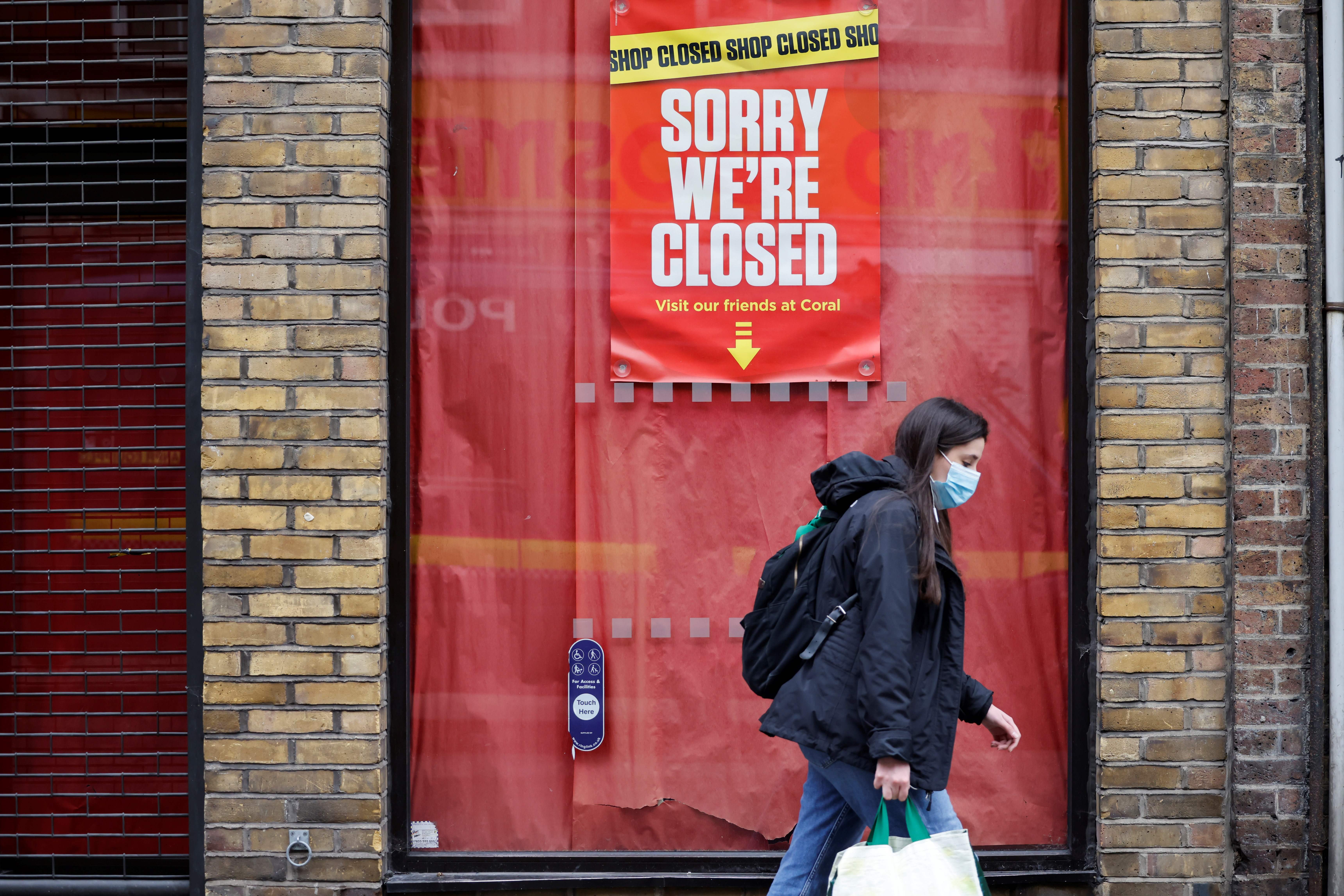A pedestrian wearing a face mask as a precautionary measure against COVID-19, walks past a closed-down shop in the City of London in January 2021