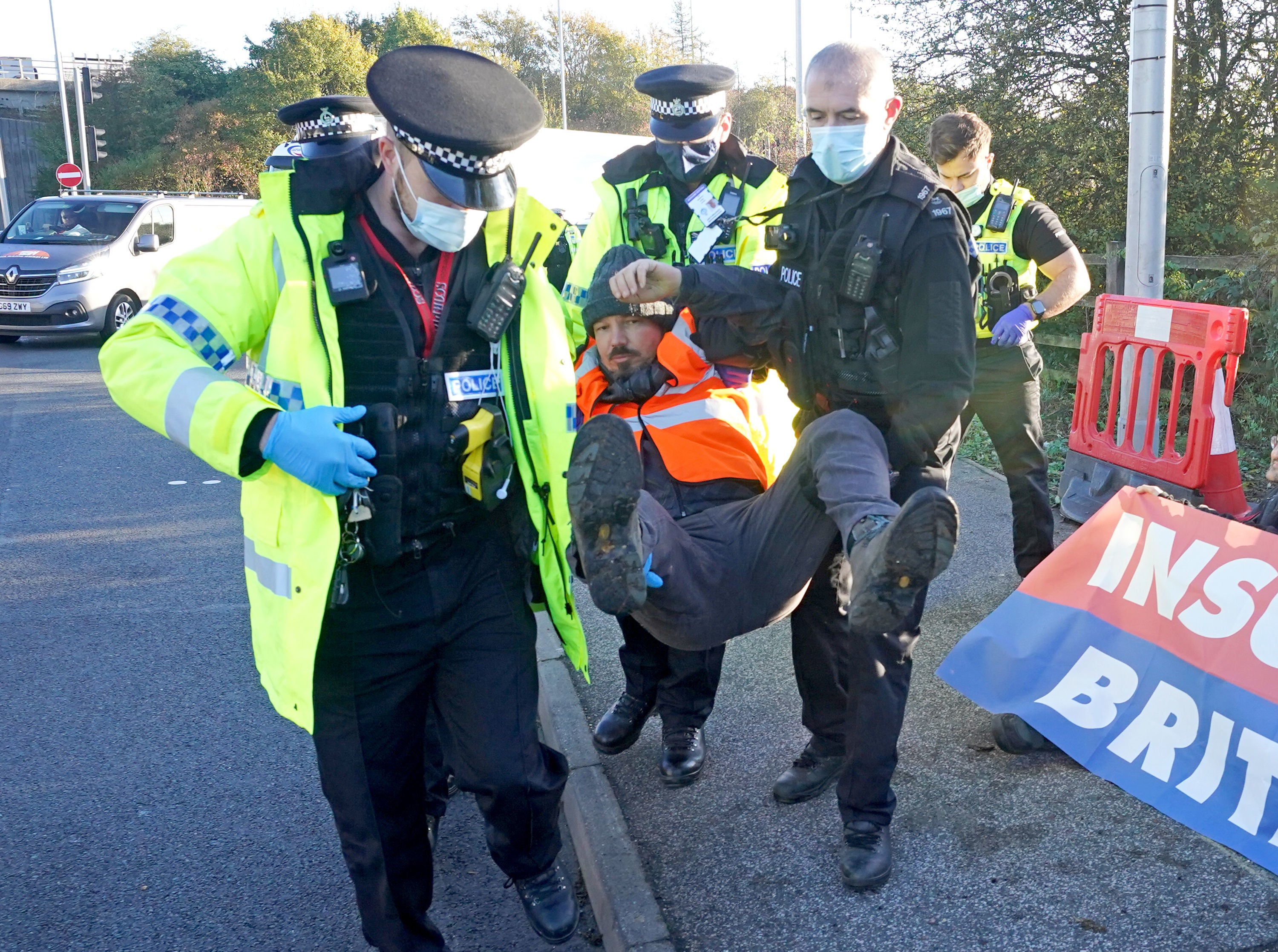 Police officers detain a protester at an Insulate Britain roadblock near to the the South Mimms roundabout at the junction of the M25 and A1.