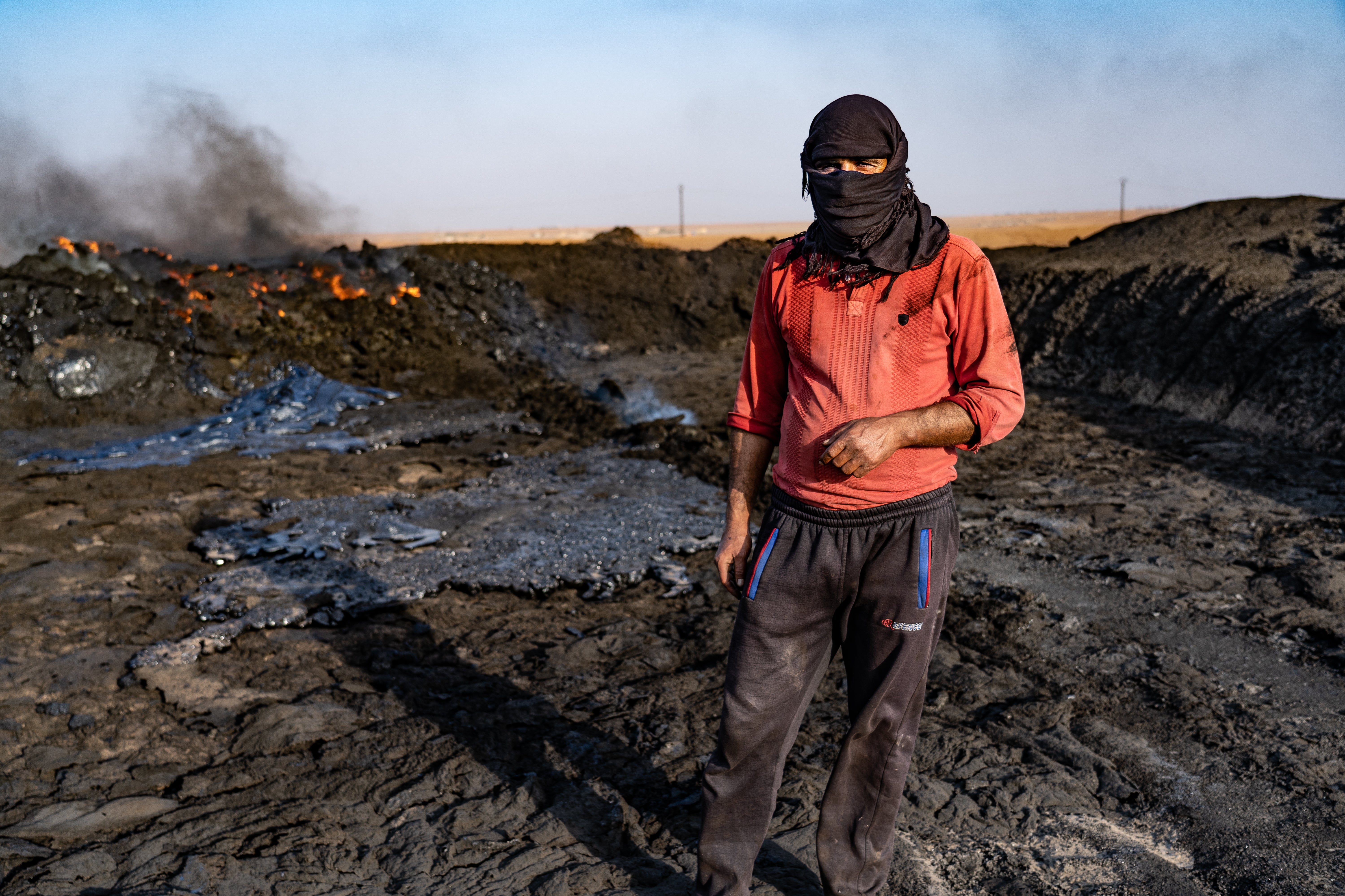 A worker at a makeshift oil refinery in northern Syria stands by a mound of oil waste