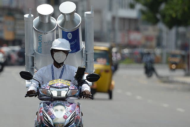 <p>A volunteer rides along a road with a mock vials of India-made vaccine Covishield and Covaxin in India</p>