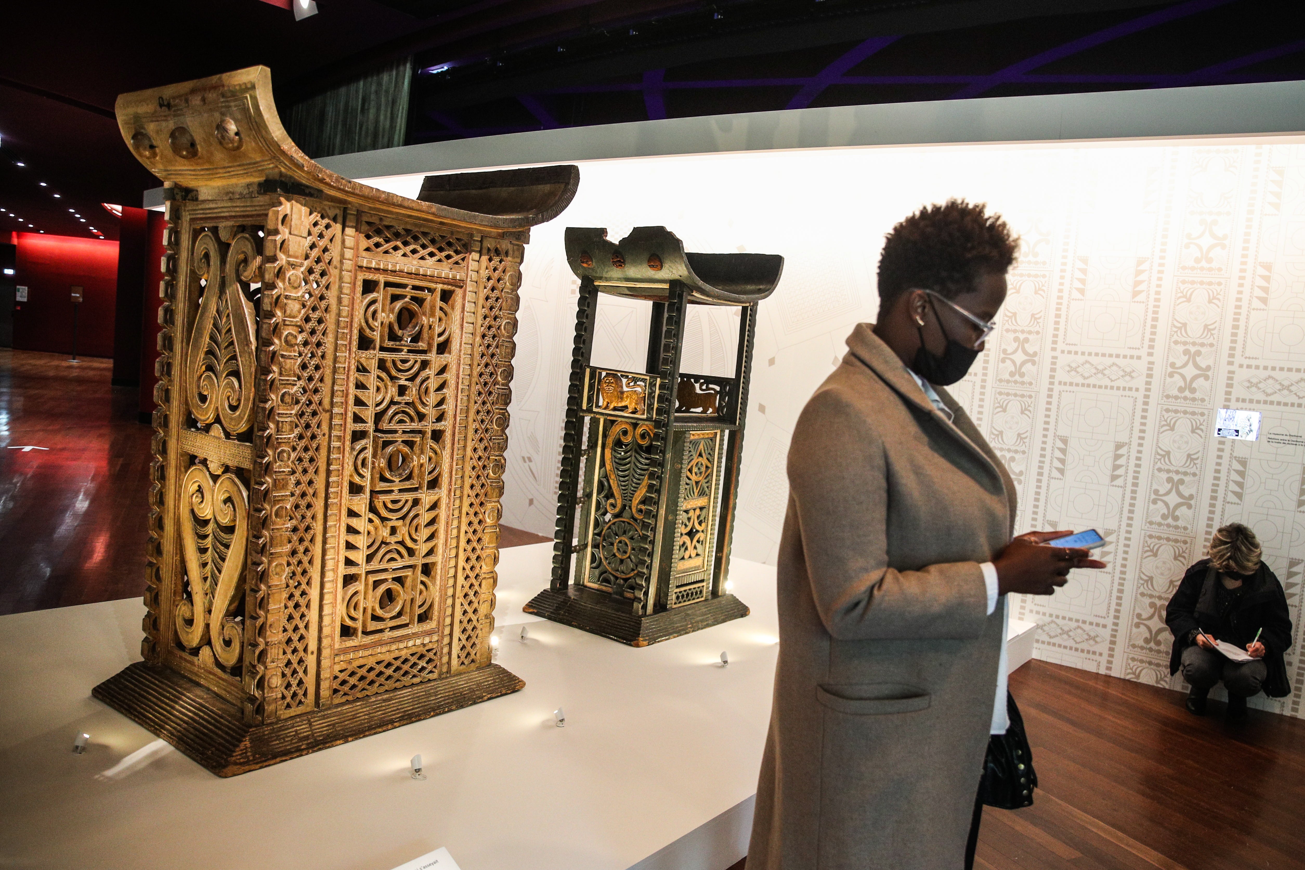A woman walks past artworks entitled ‘The throne of King Ghezo’ (left) and ‘The throne of King Glele’