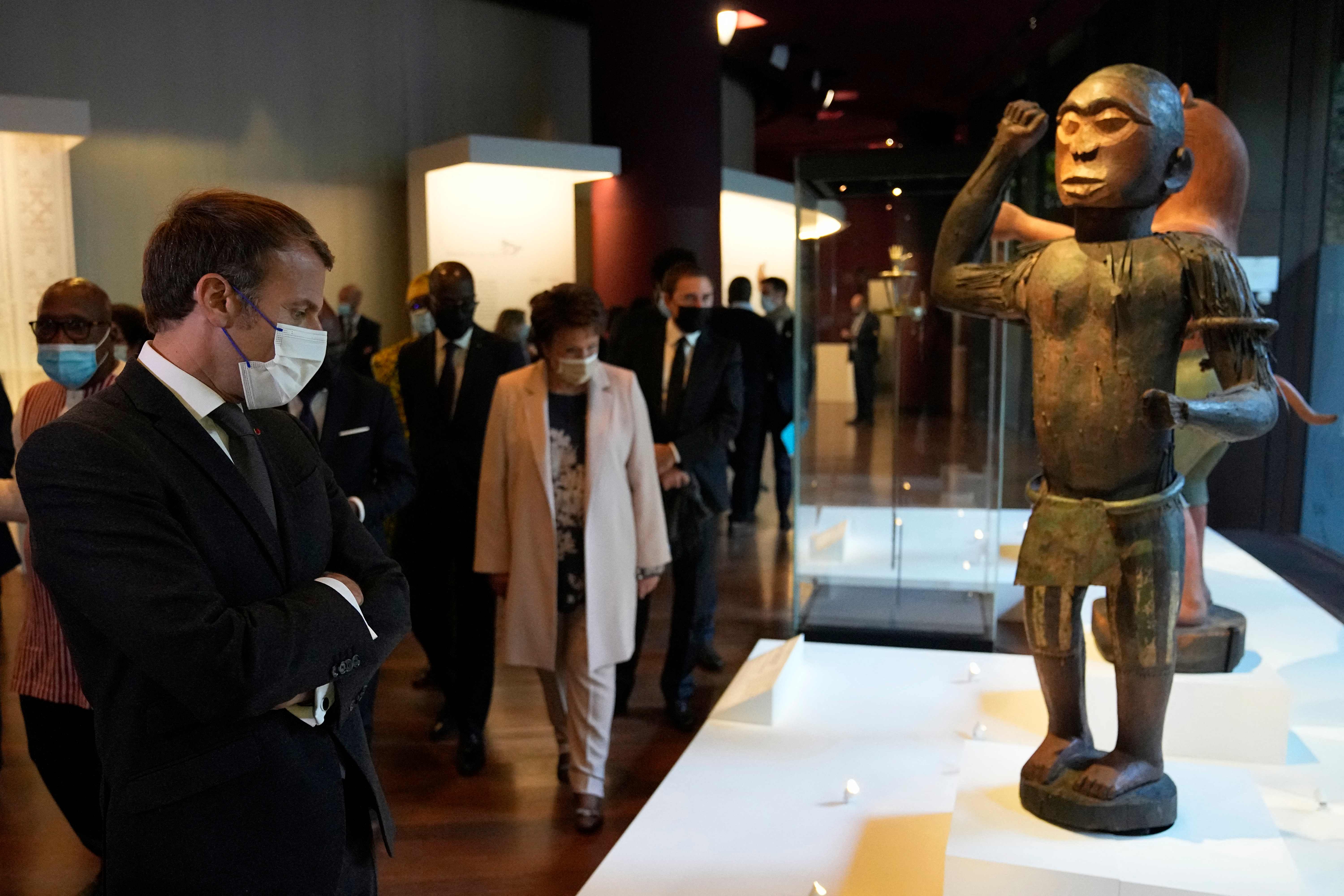 French President Emmanuel Macron watches a 19th century royal statue of a half-man half-bird representing Benin's King Ghezo