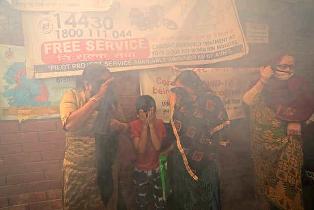 <p>A family walks past smoke from fumigation in a densely populated area of Delhi</p>