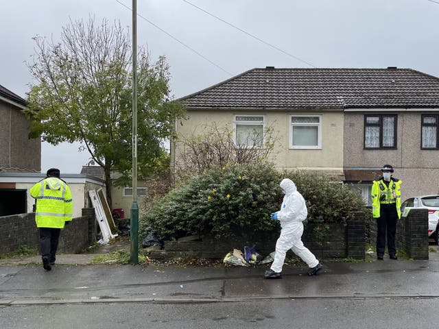 <p>Police and forensics walk past flowers left outside the house in Pentwyn, Penyrheol, where 10-year-old Jack Lis was killed by a dog</p>