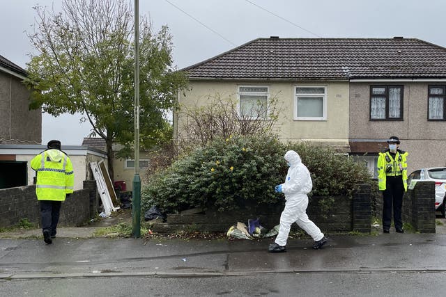 <p>Police and forensics walk past flowers left outside the house in Pentwyn, Penyrheol, where 10-year-old Jack Lis was killed by a dog</p>
