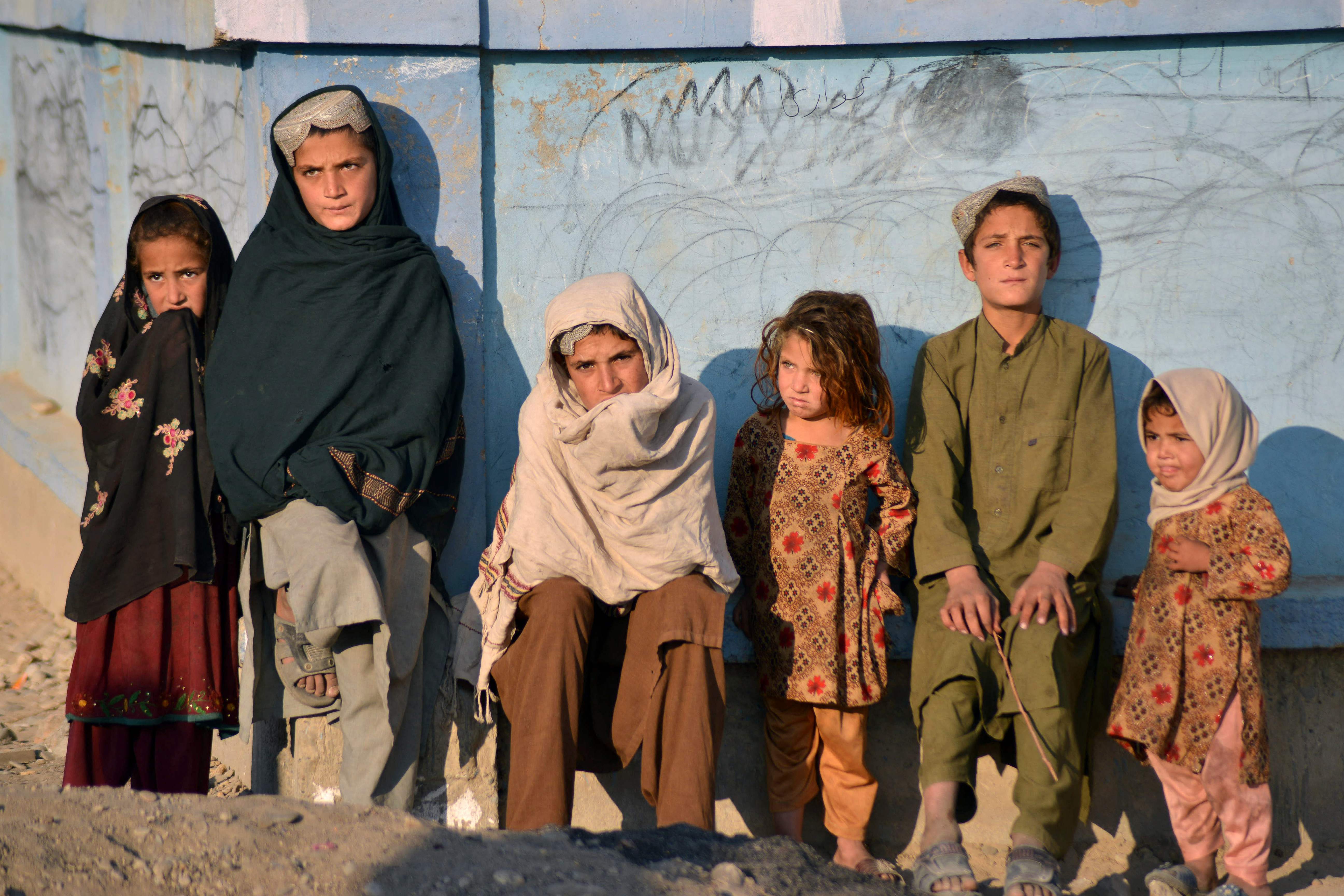Children bask in the sun next to a wall along a street in Nad Ali district, Helmand province, on Wednesday
