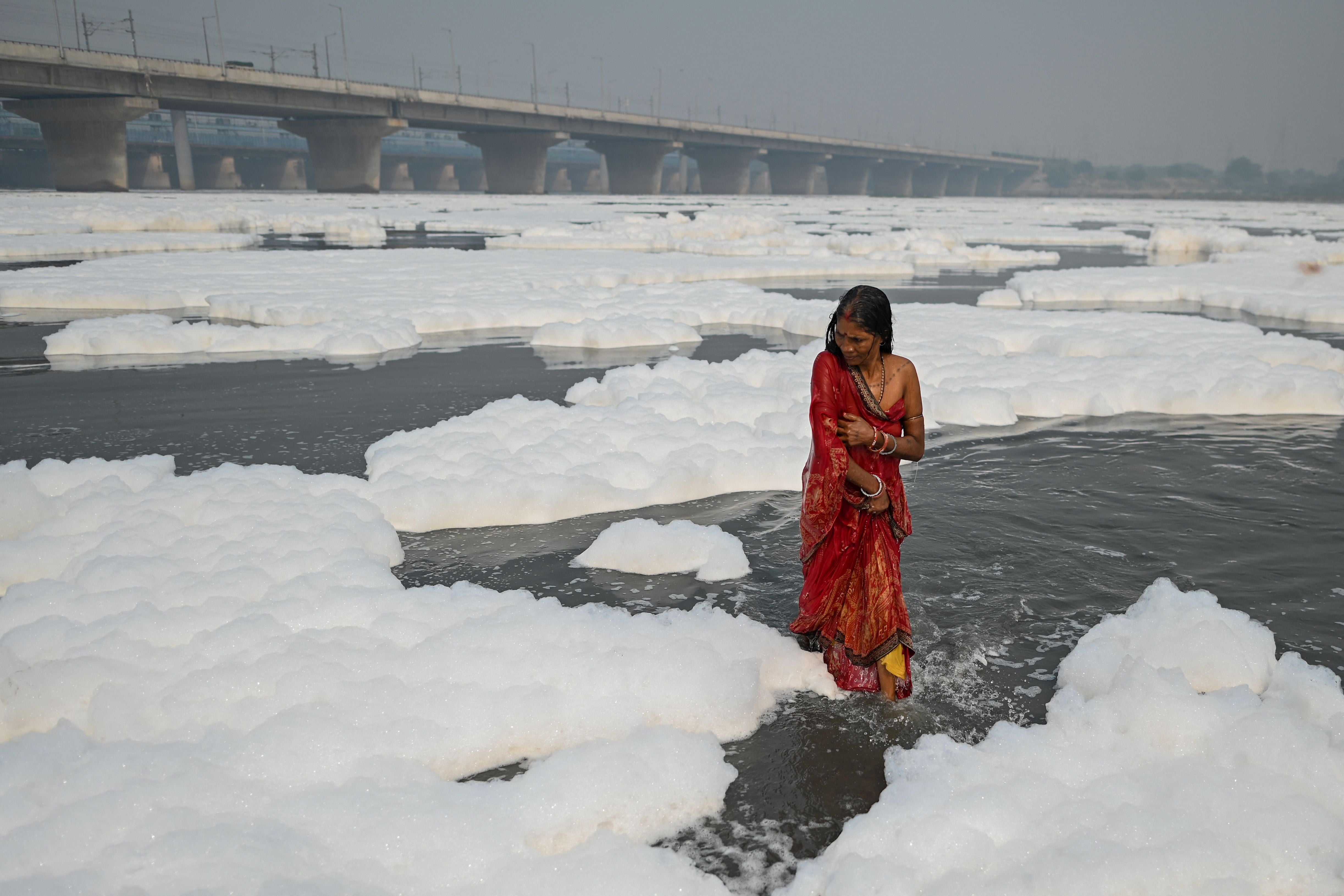 A devotee stands by foam in the Yamuna river as part of rituals for the festival of Chhath