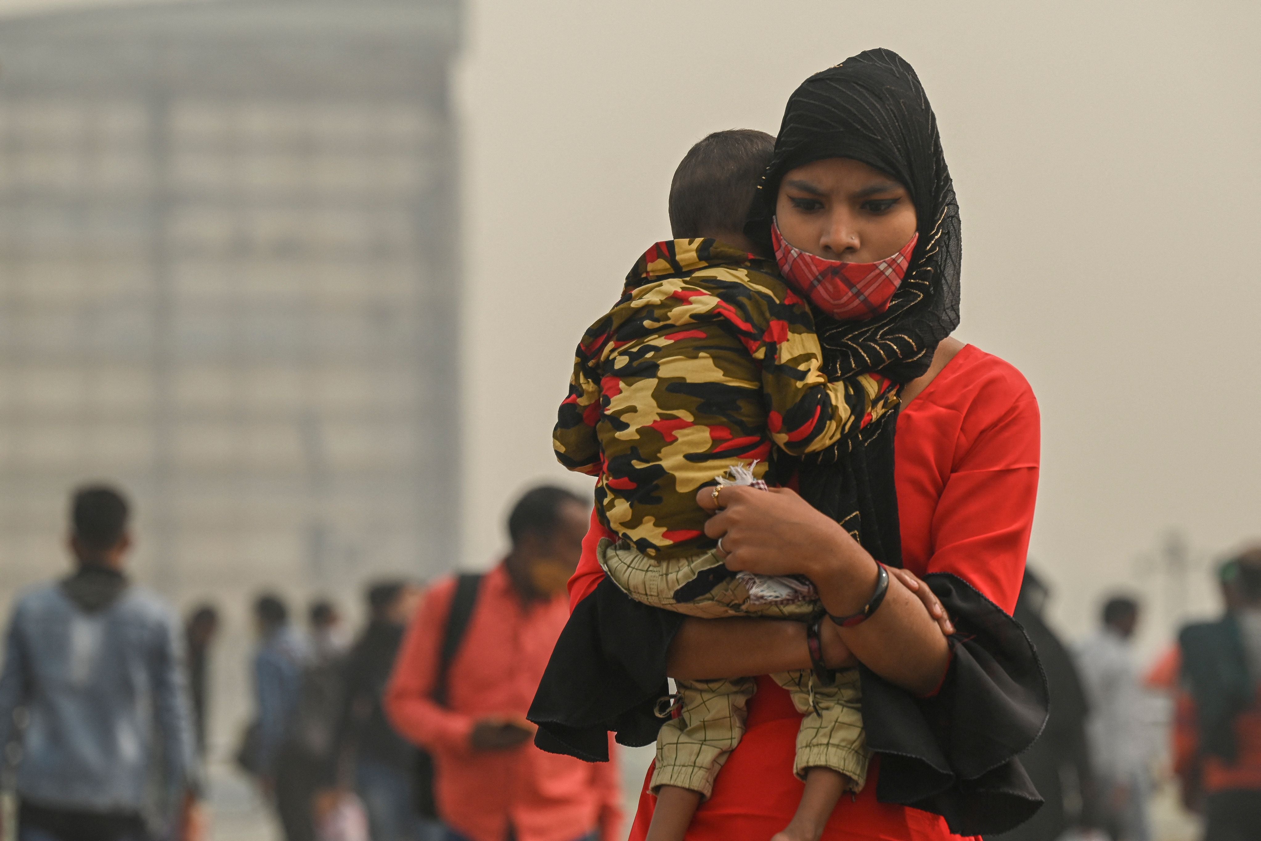 A woman carrying a child walks across a footbridge under heavy smoggy conditions in Delhi on 12 November, 2021