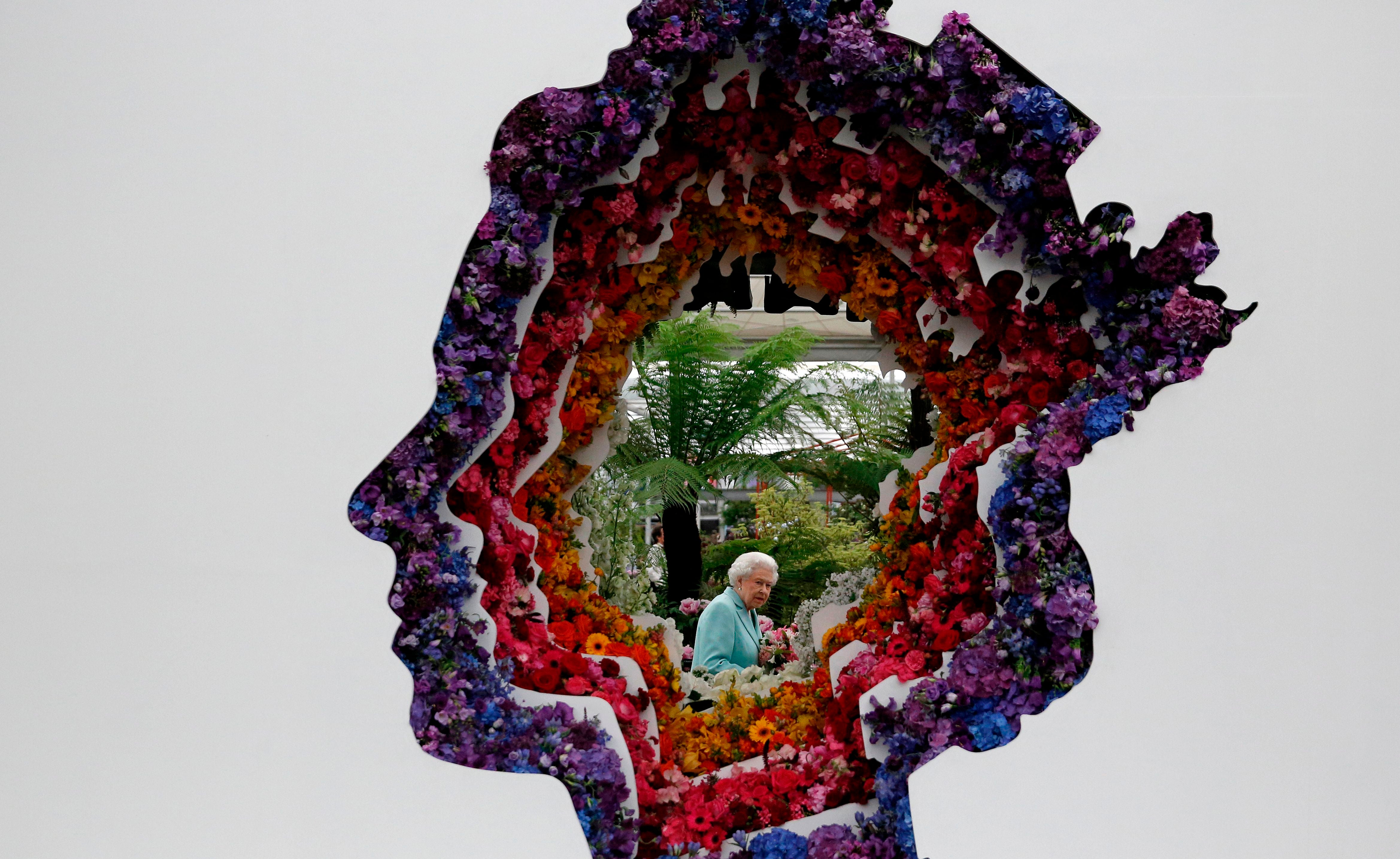 Queen Elizabeth II pictured through a gap in a floral exhibit by the New Covent Garden Flower Market, which features an image of the Queen, during a visit to the 2016 Chelsea Flower Show