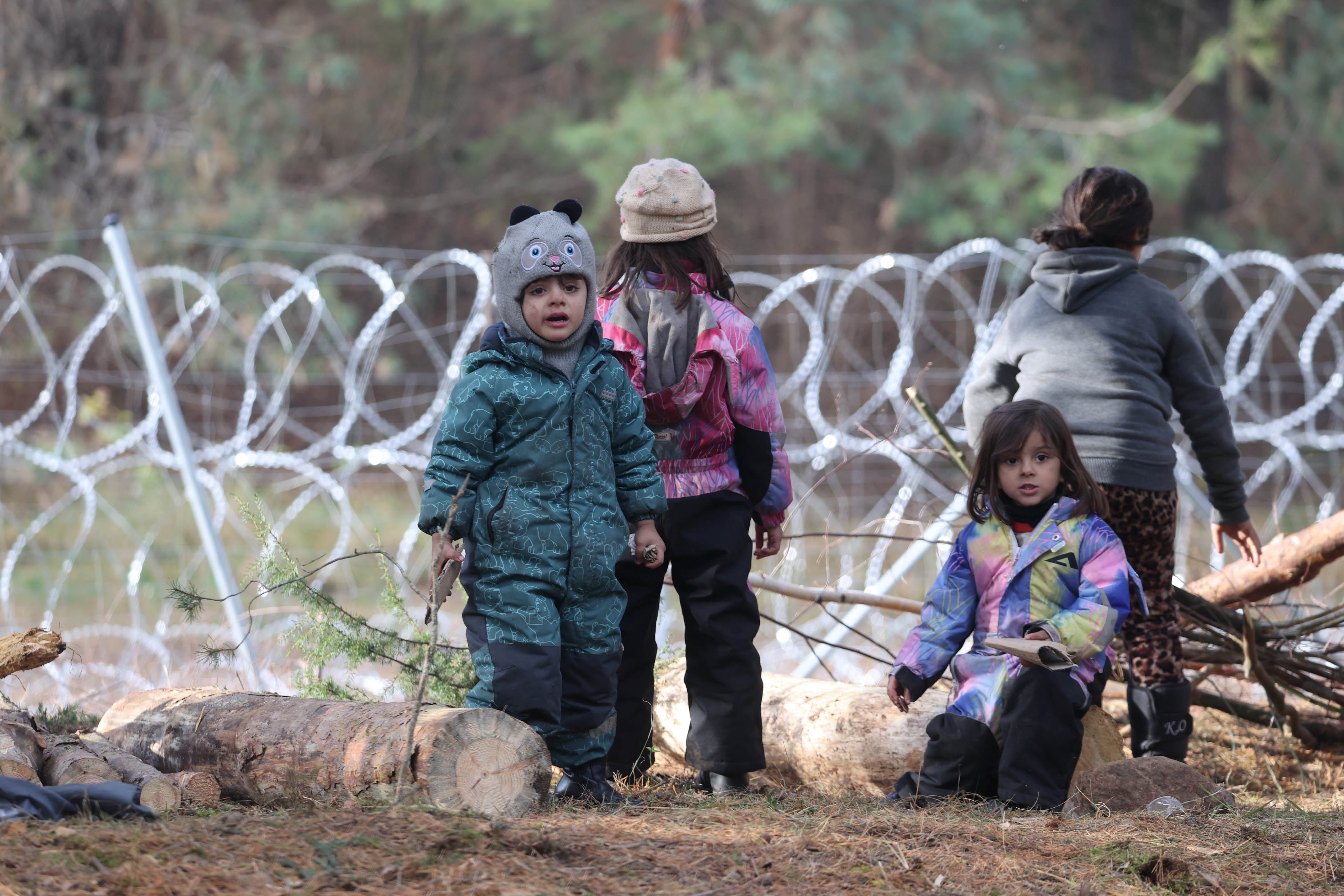 Children gather near a barbed wire fence in a migrants’ makeshift camp