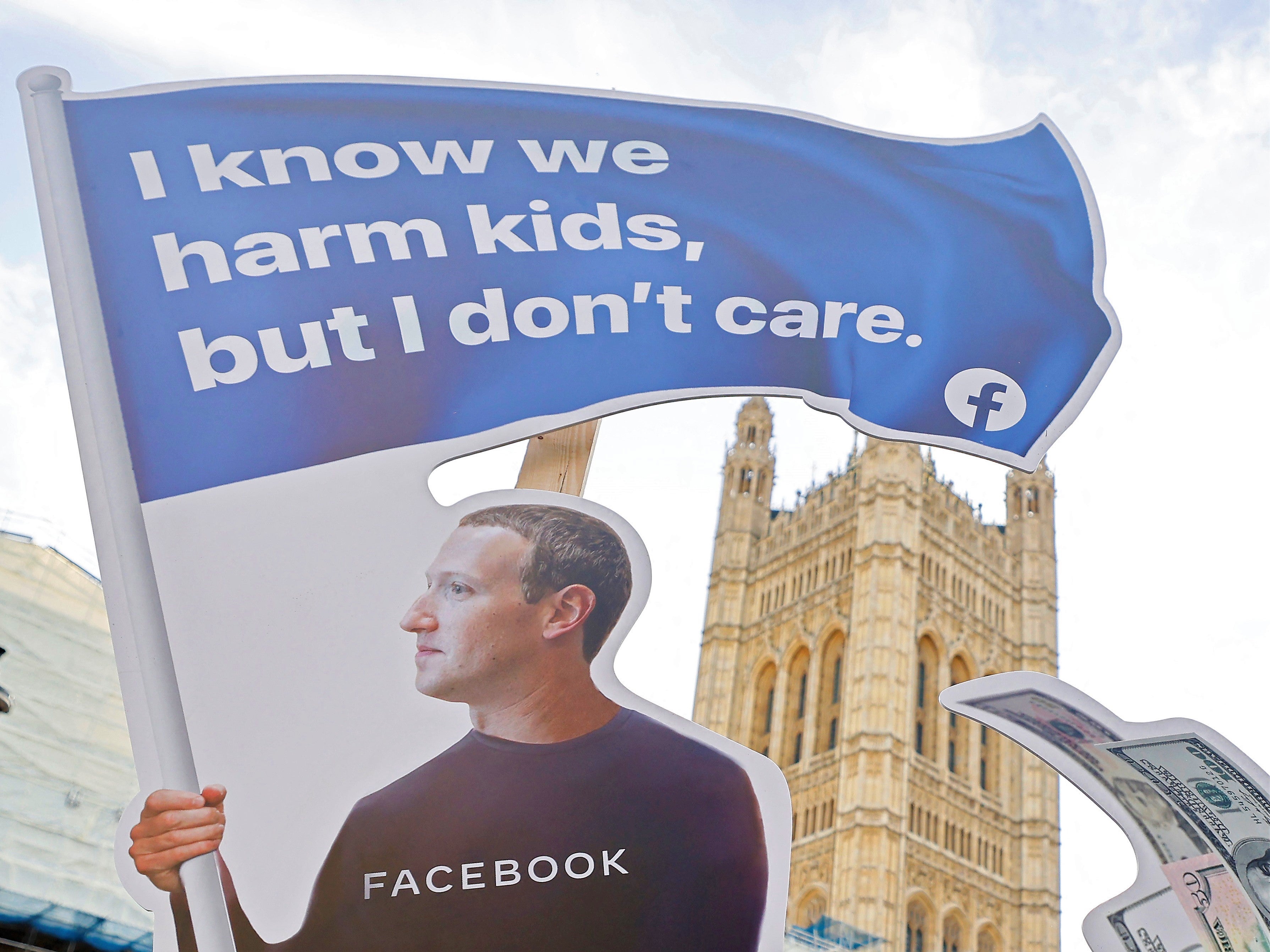 A demonstrator poses with an installation depicting Facebook founder Mark Zuckerberg surfing on a wave of cash and surrounded by distressed teenagers, during a protest opposite the Houses of Parliament in central London on October 25, 2021