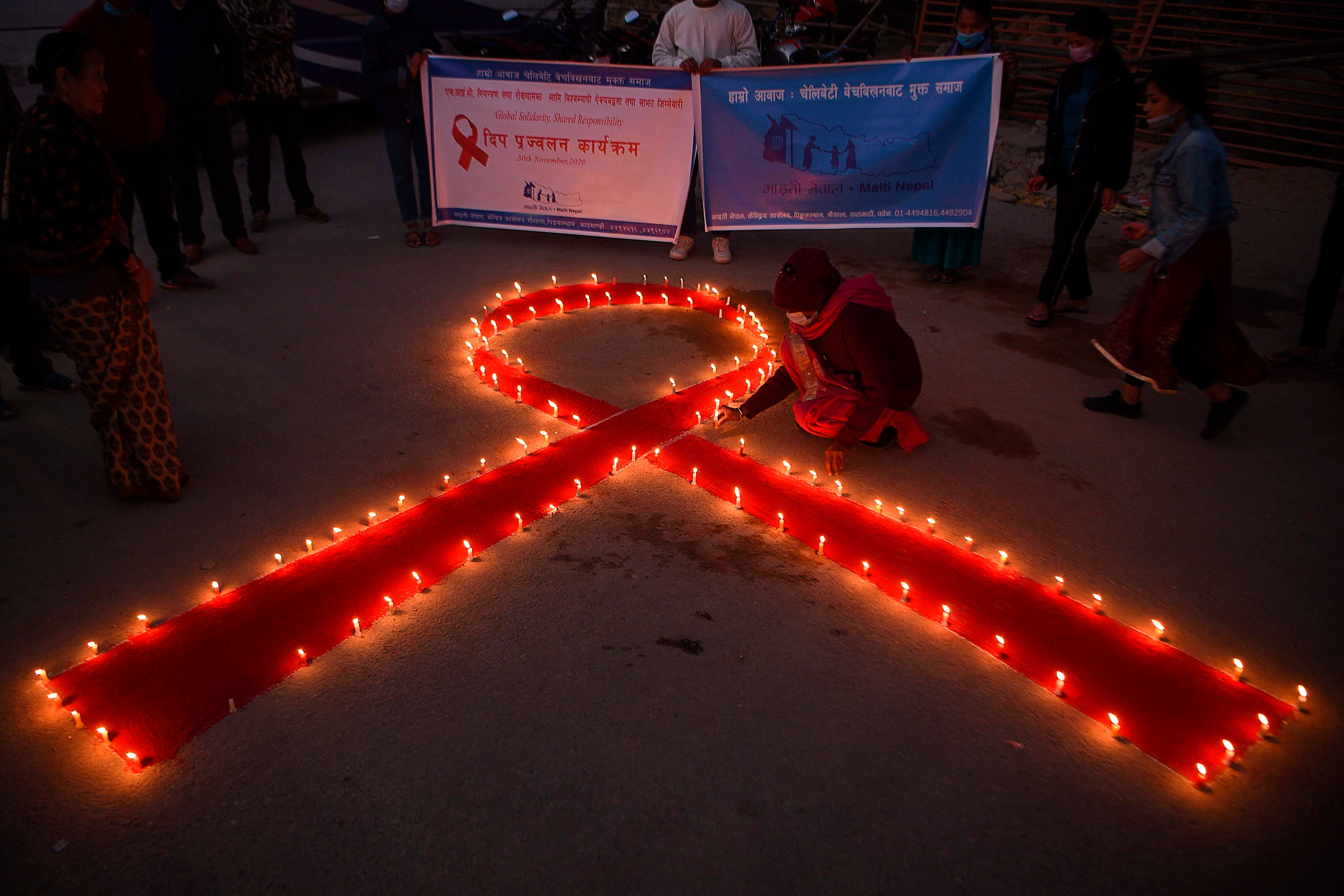 File: A volunteer lights candles forming the shape of a red ribbon during an awareness event on the eve of the World AIDS Day