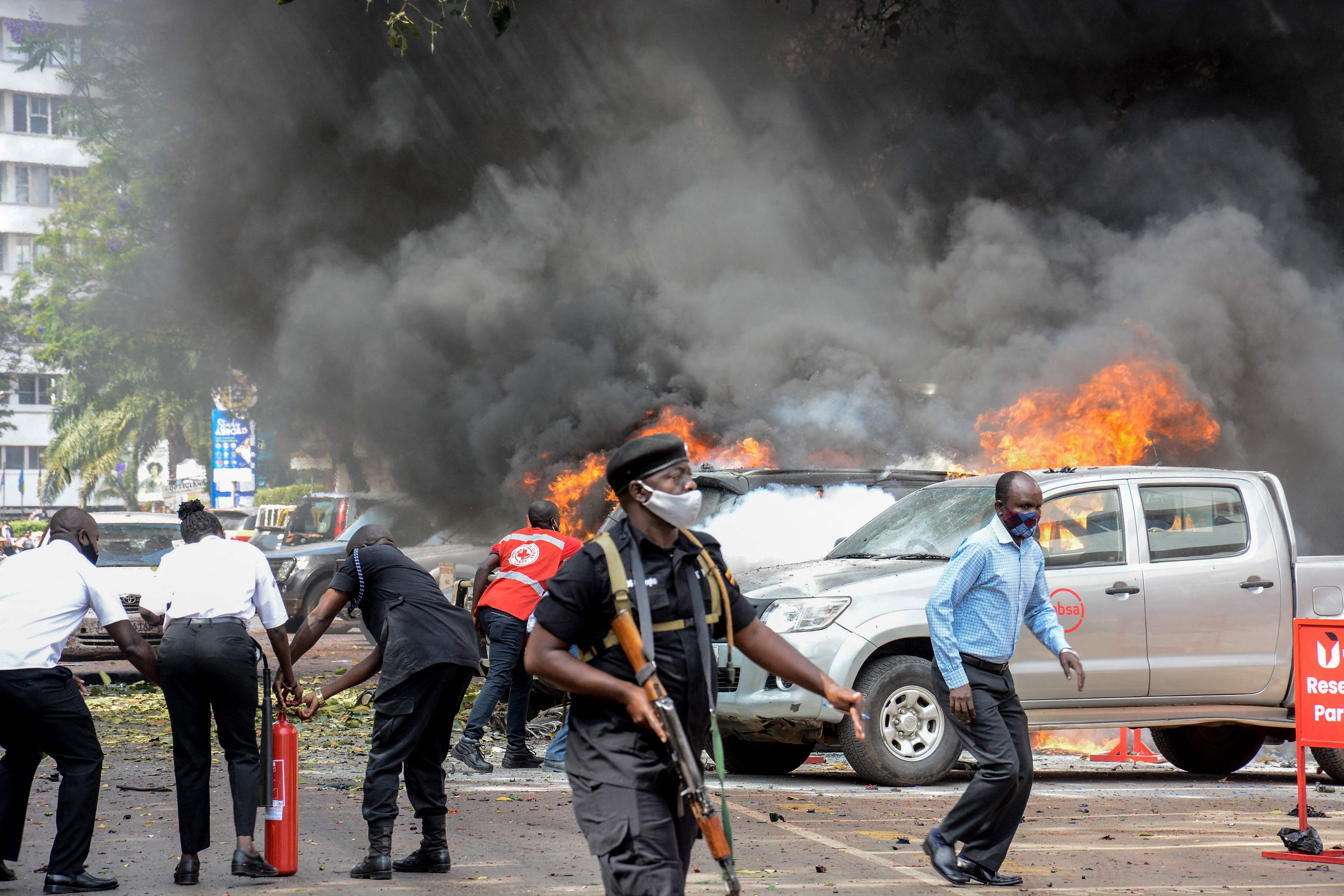 People extinguish fire on cars caused by a bomb explosion near Parliament building in Kampala, Uganda