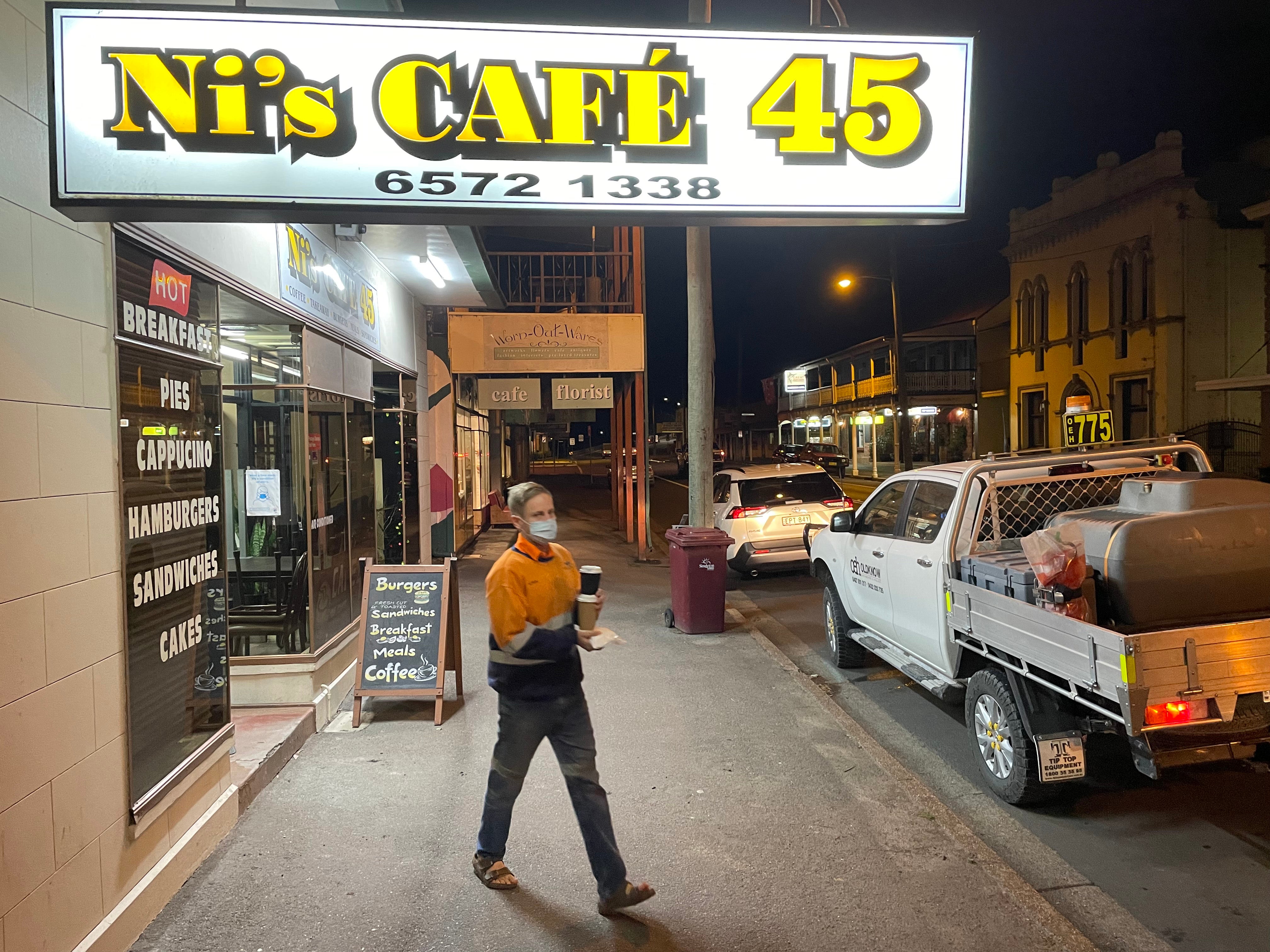 Mine workers in bright yellow and orange clothes grab coffee in the pre-dawn dark in downtown Singleton