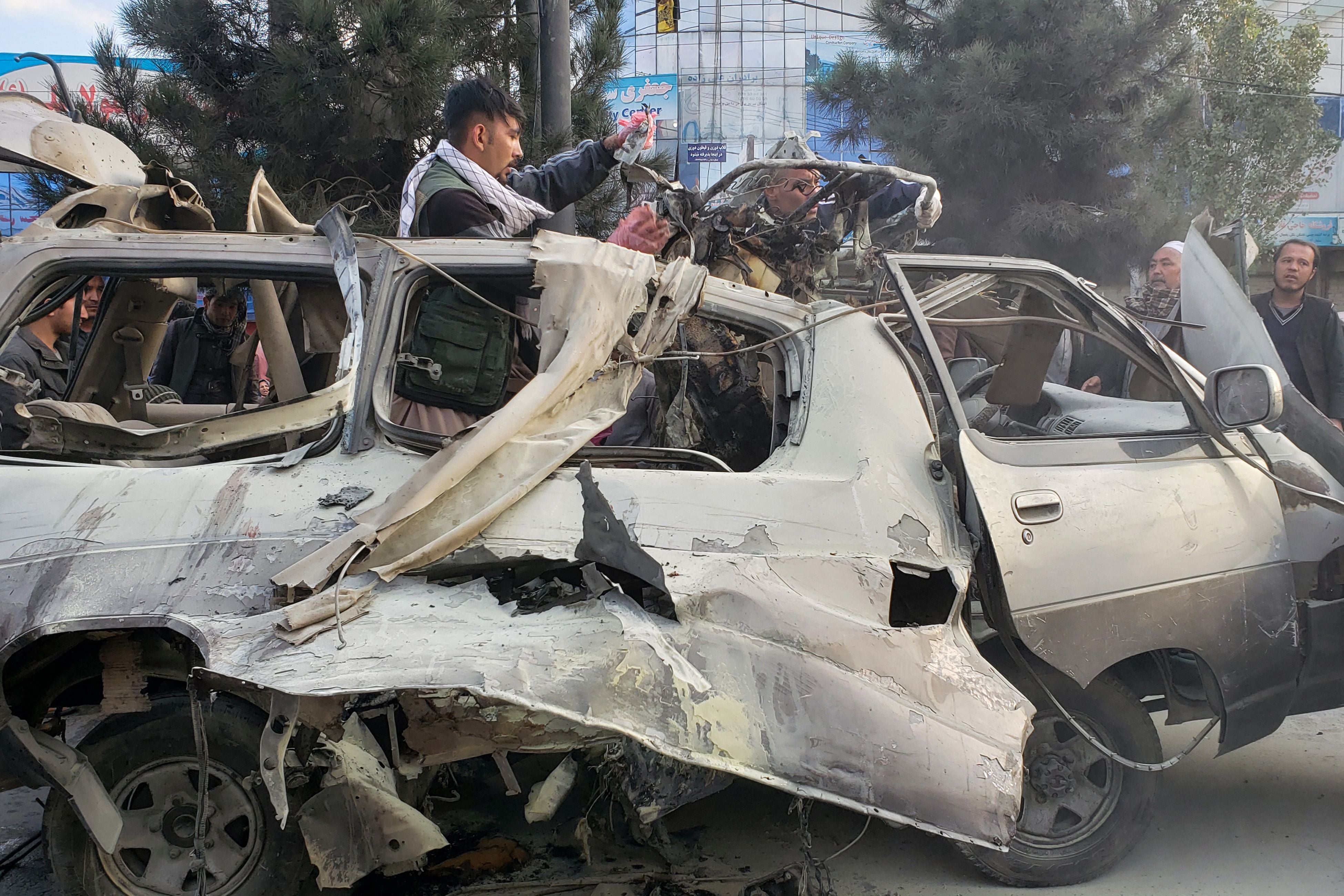 Residents gather next to a damaged minibus after a bomb blast where two people were killed and five wounded in Kabul on November 17, 2021.
