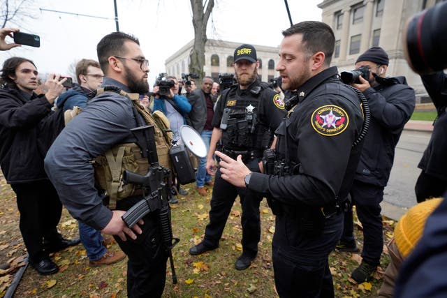 <p>A Kenosha County Sheriffs Department officer questions a protester carrying a rifle outside the Kenosha County Courthouse on Wednesday morning</p>