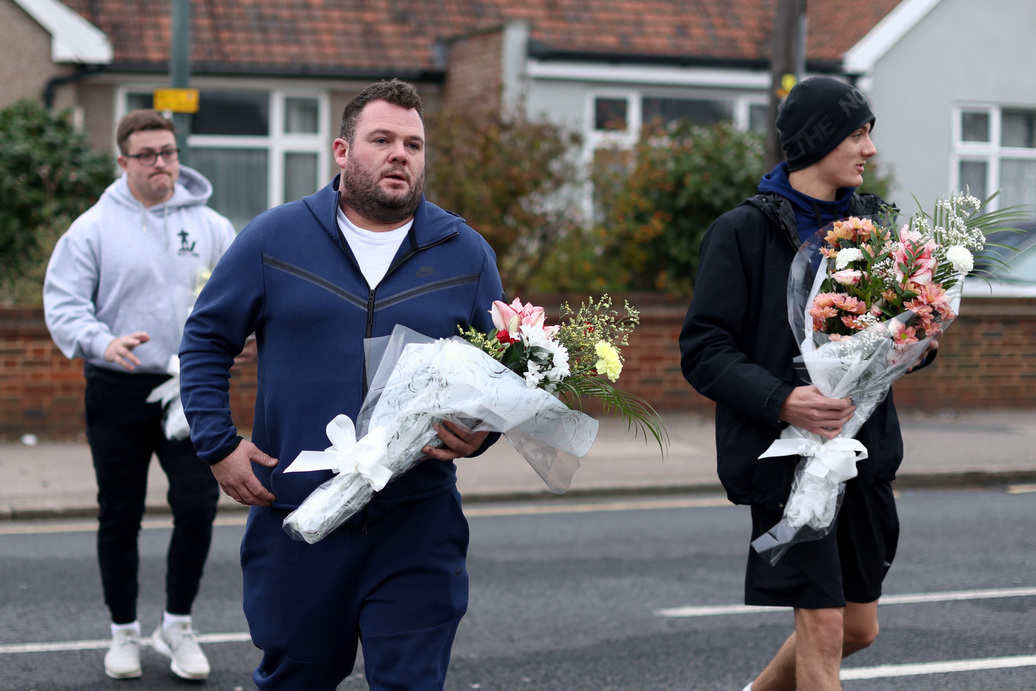People carry flowers to lay at the scene of a house fire