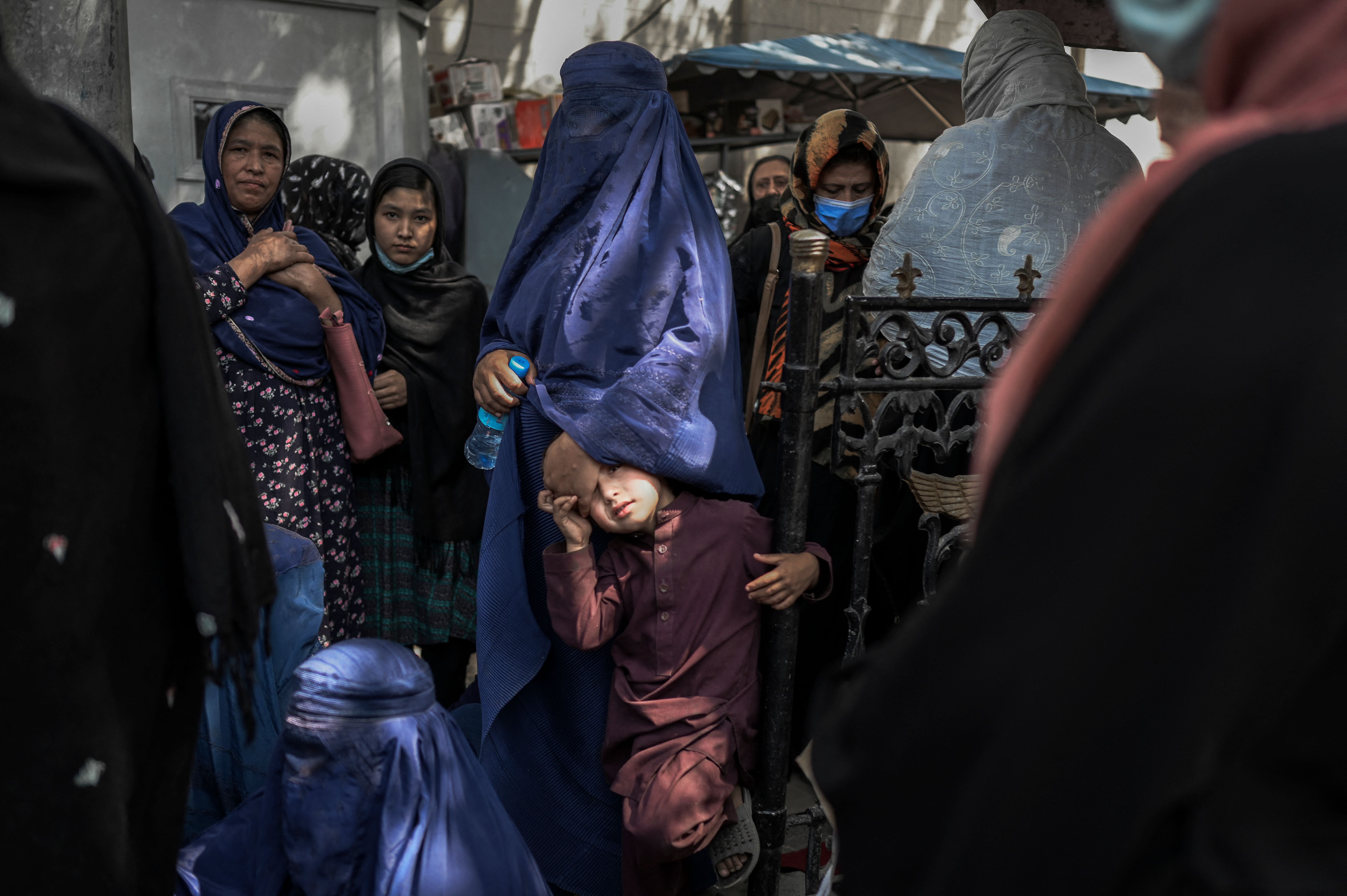 Women wait in front of a bank to withdraw money in Kabul