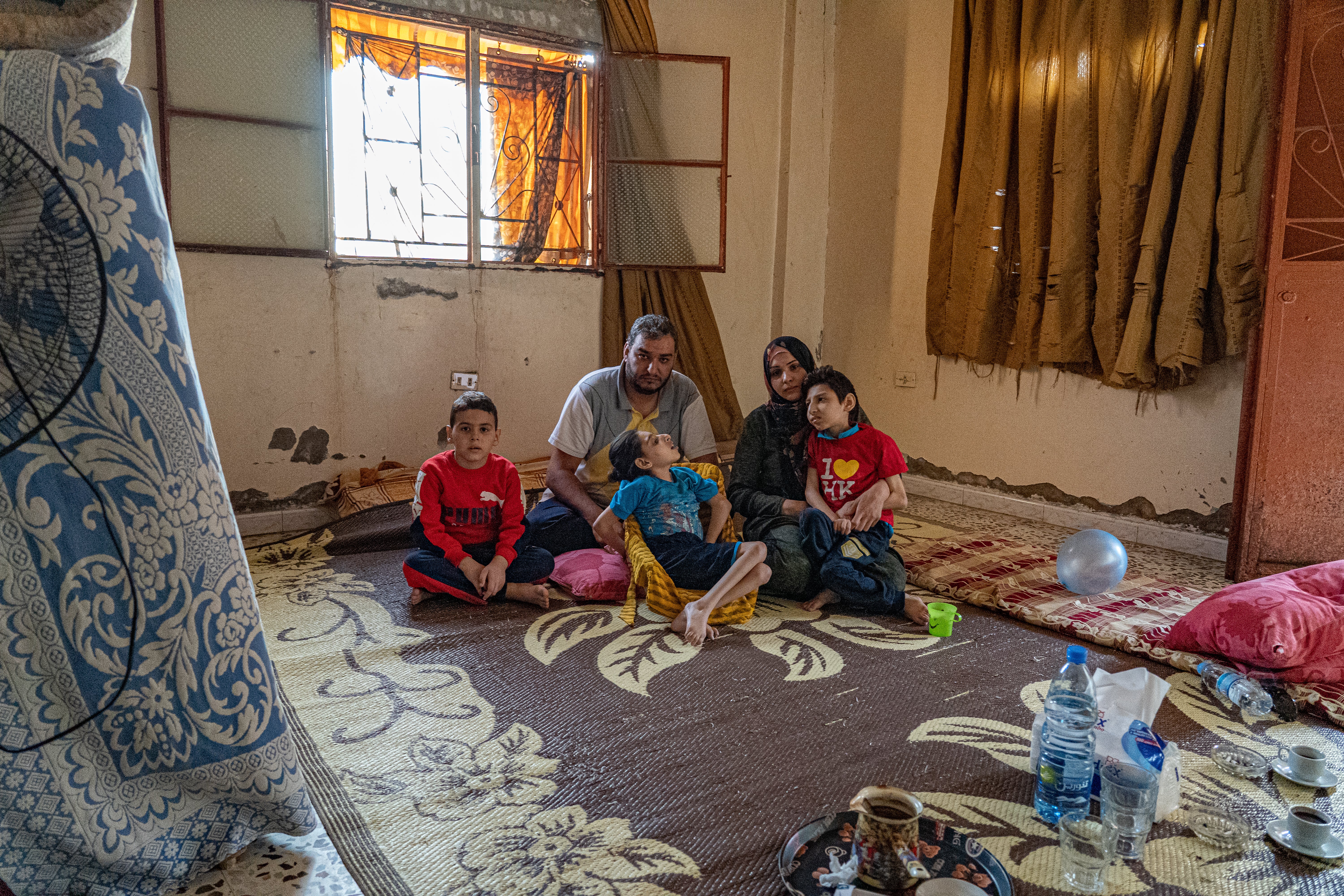 Hanan and her family sit on the floor of one of the two rooms they live in