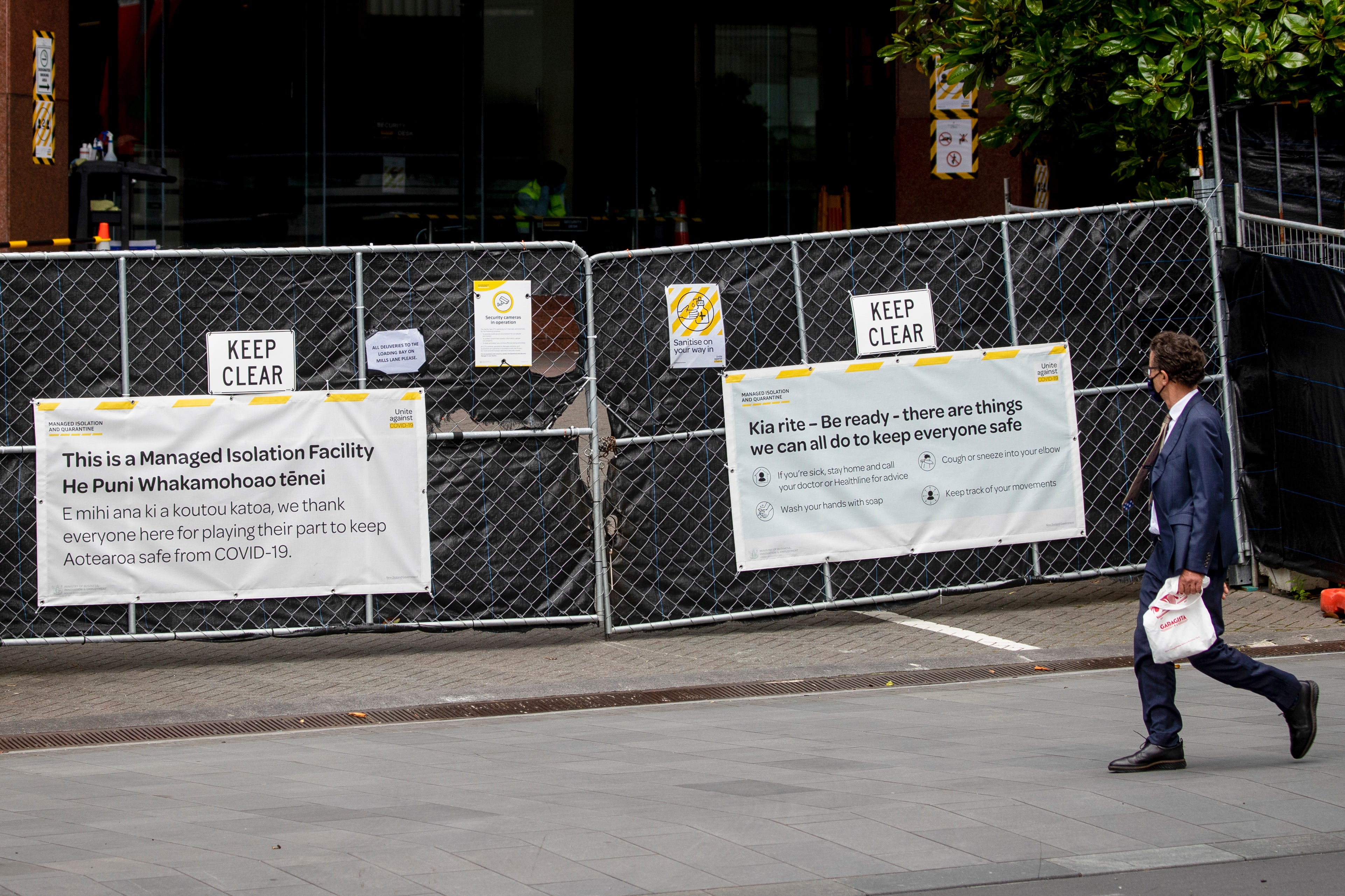 A man walks past the gates to a government-managed isolation facility in Auckland