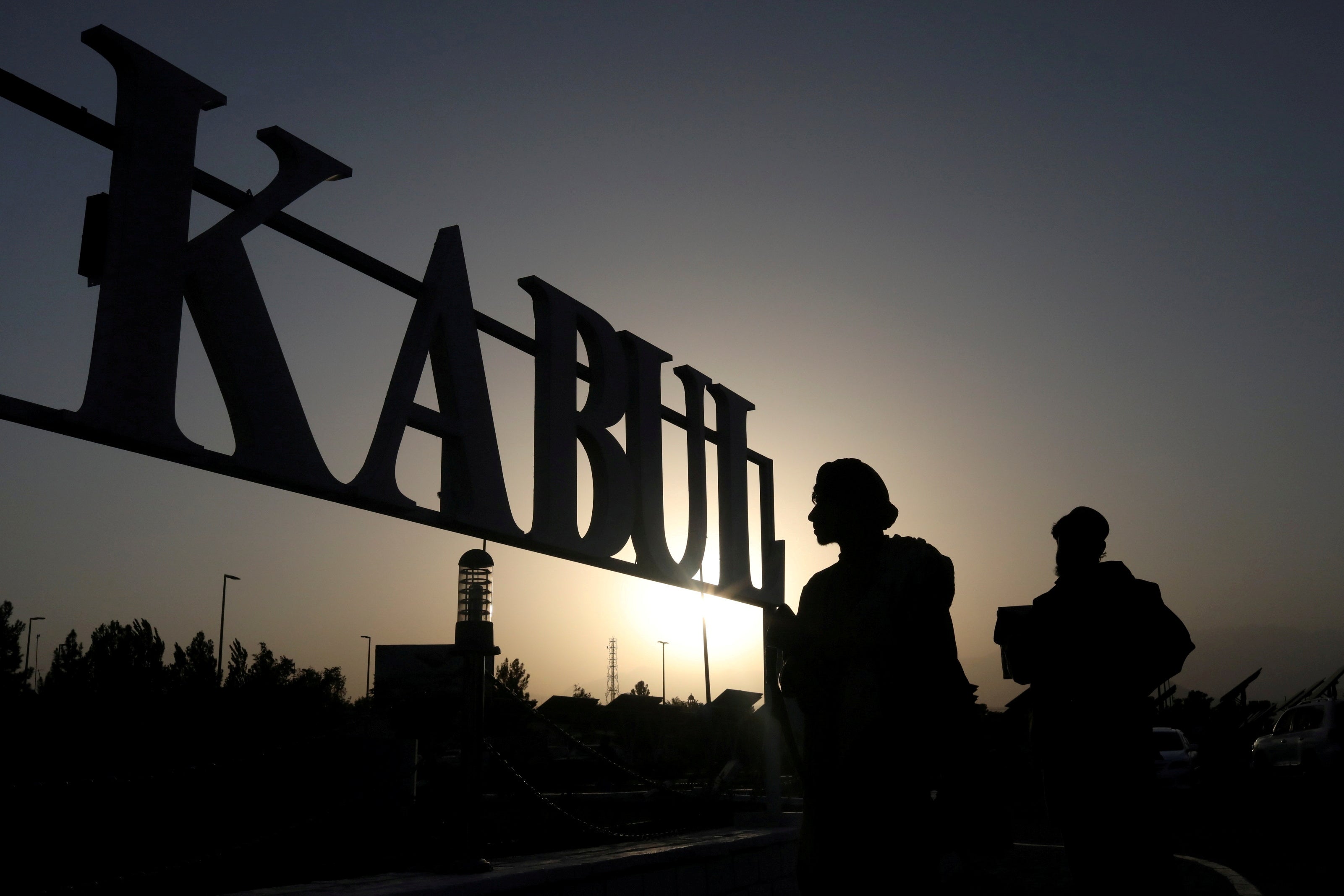 Taliban soldiers stand in front of a sign at the international airport in Kabul, Afghanistan
