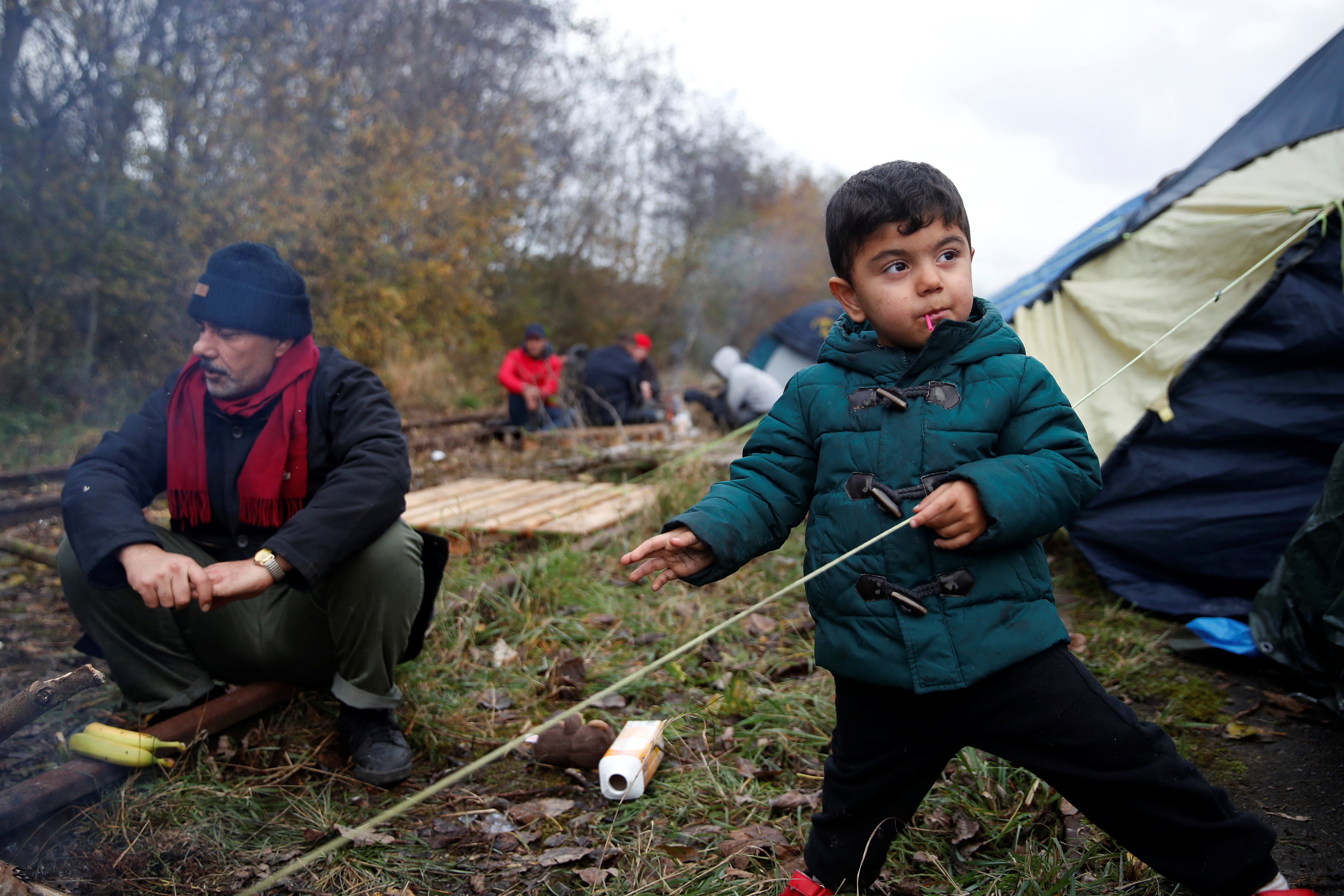 Migrants stand near a tent at a makeshift migrant camp in Loon Beach