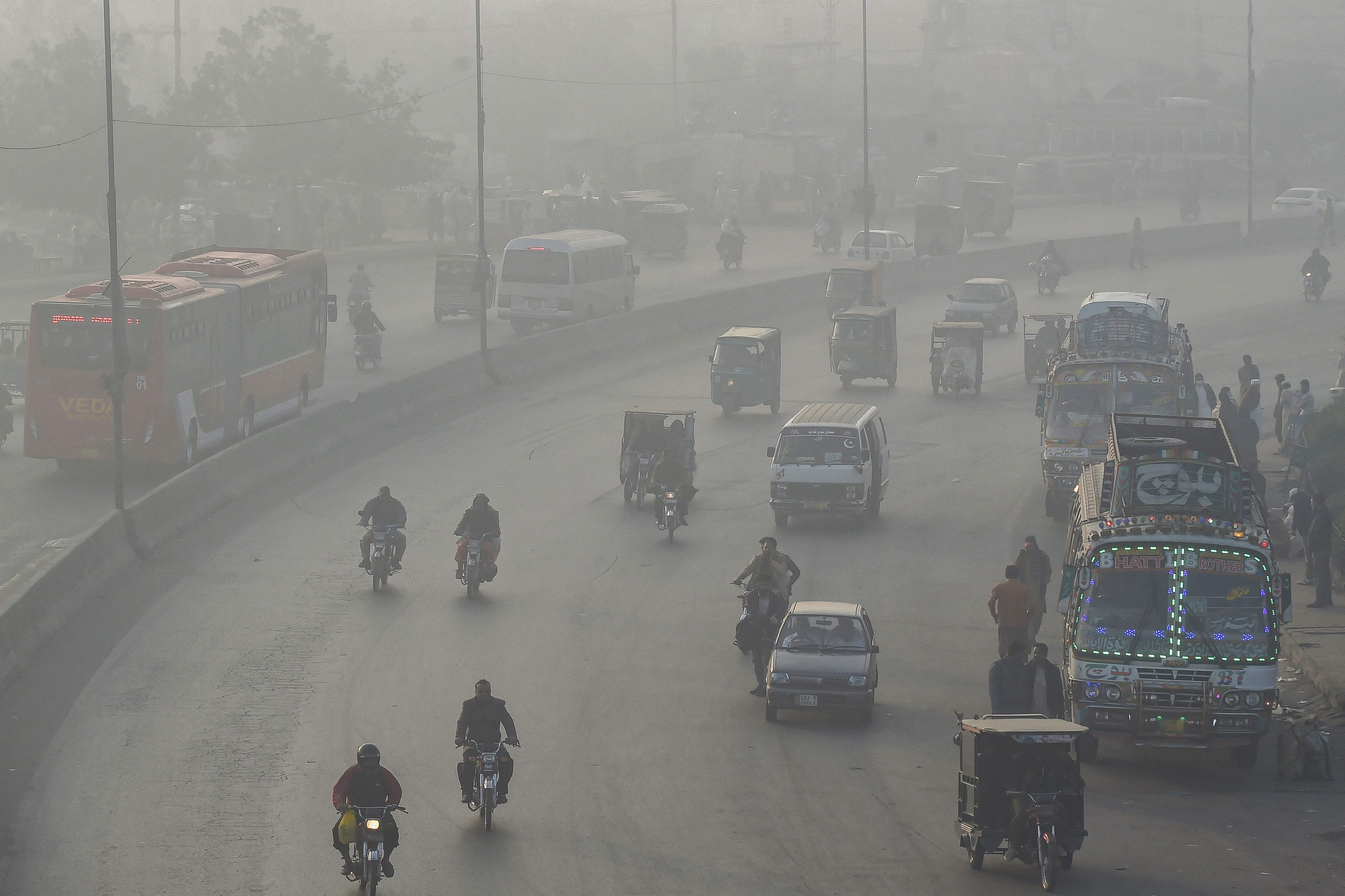In this picture taken on 24 November 2021, commuters make their way along a road amid smoggy conditions in Lahore