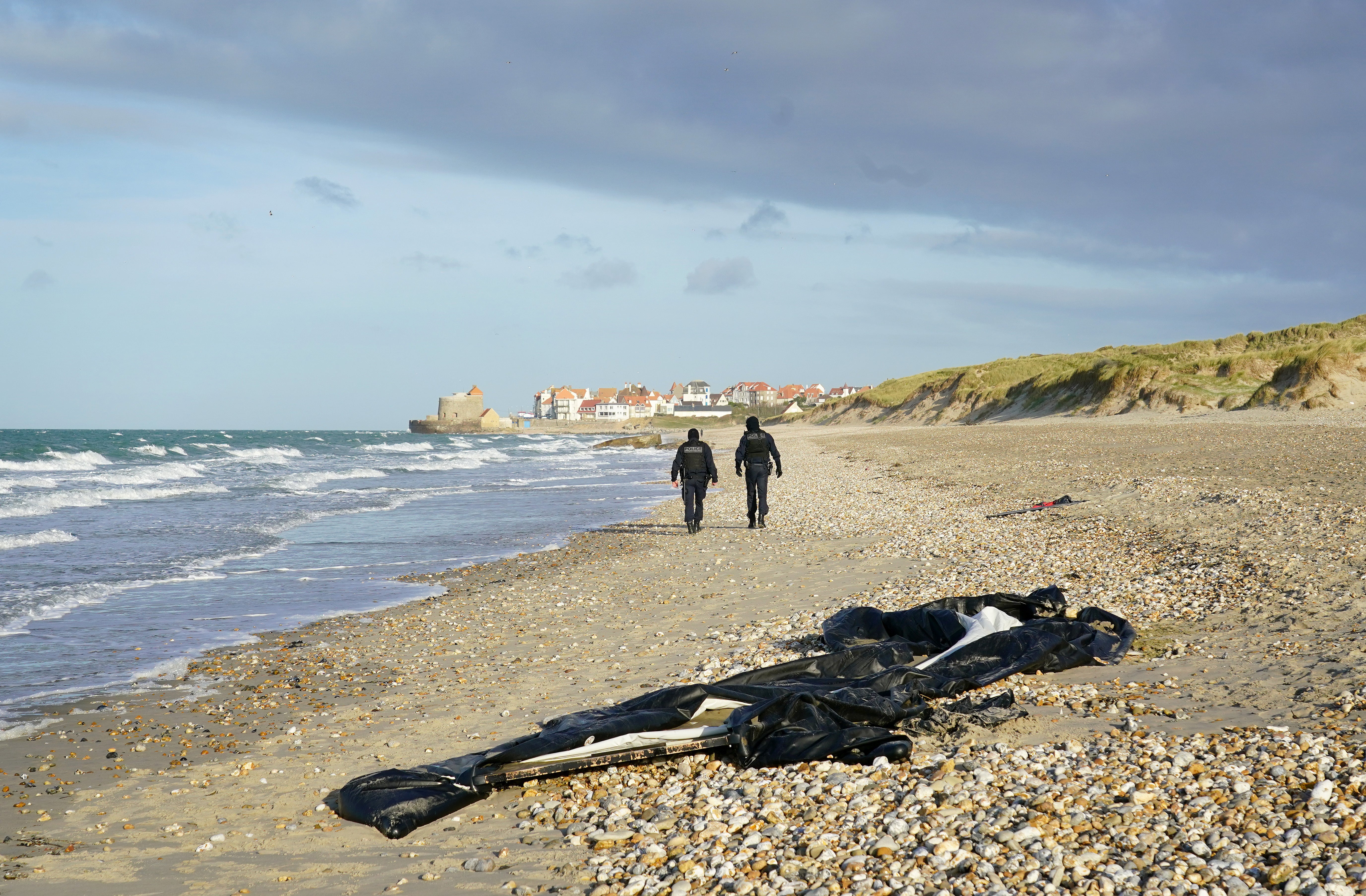 French police officers pass a deflated dinghy on the beach in Wimereux near Calais