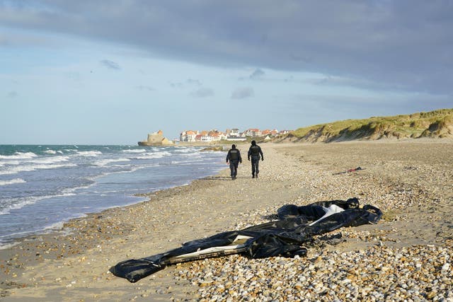 <p>French police officers pass a deflated dinghy on the beach in Wimereux near Calais</p>