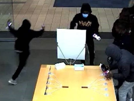 A grainy still from CCTV footage shows four young figures in hoodies and jeans in the midst of a robbery