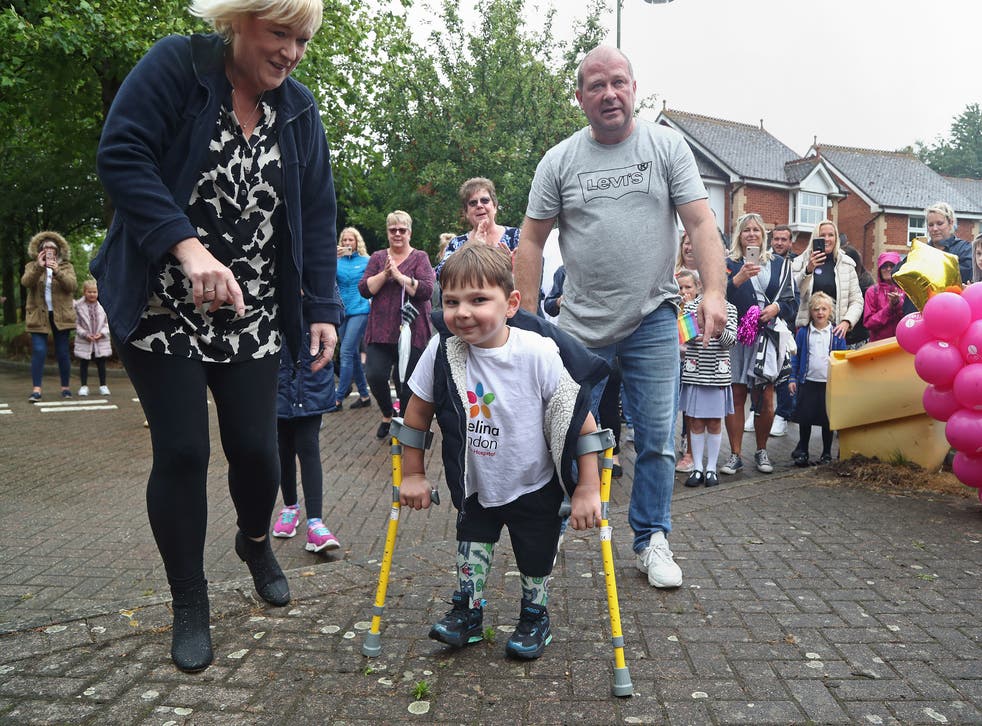 <p>Tony Hudgell, who uses prosthetic legs, takes the final steps in his fundraising walk in West Malling, Kent, with adoptive parents Paula and Mark</p>