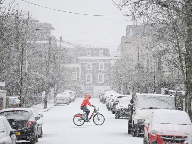 <p>A cyclist crosses a snow covered road in west London</p>