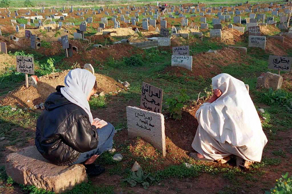 A woman, right, prays on the grave of her son and grandson killed during the massacre of Rais in 1997