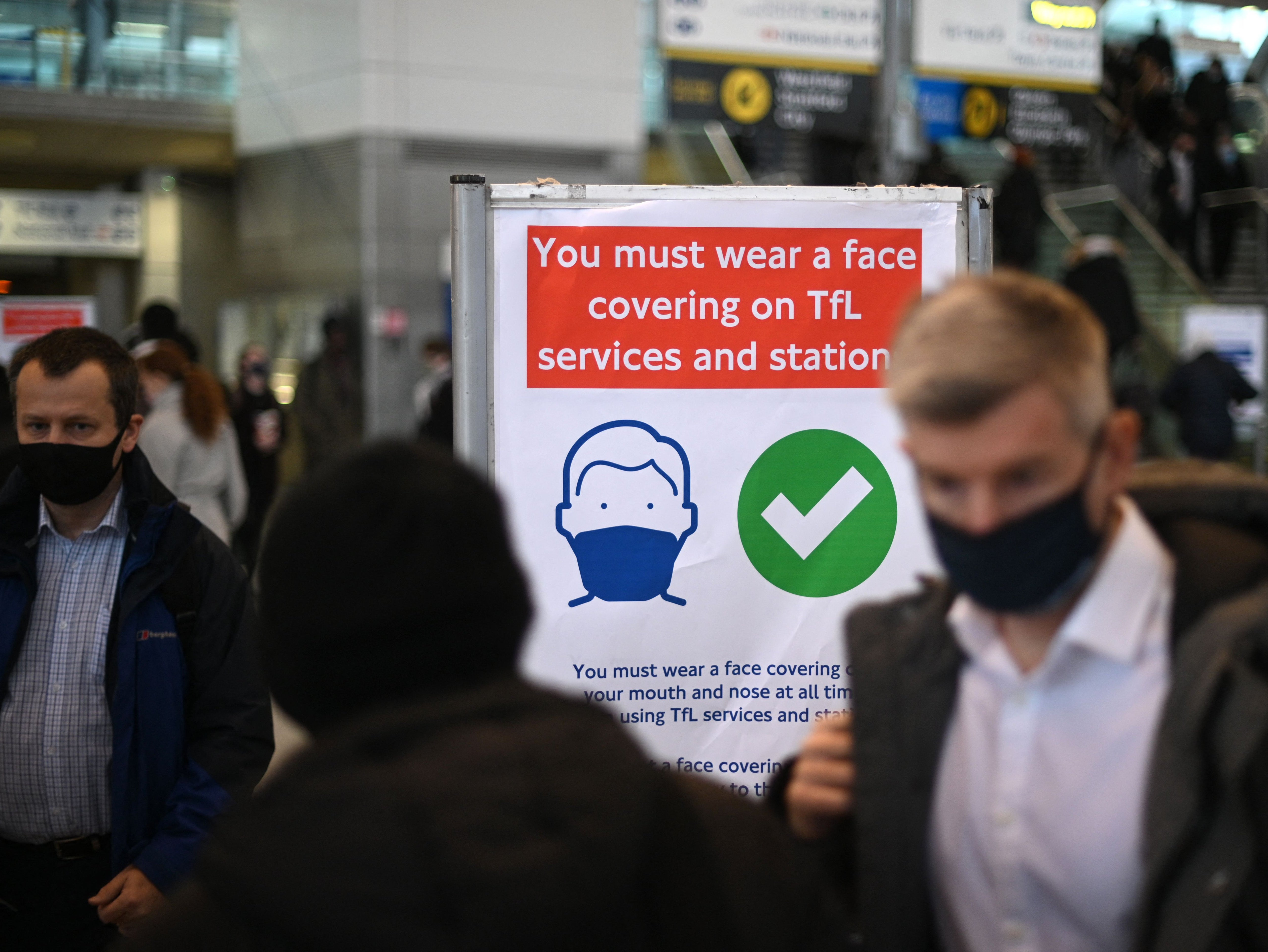 Commuters walk past a notice board reminding them of wearing face coverings at Stratford Tube station in east London on 1 December