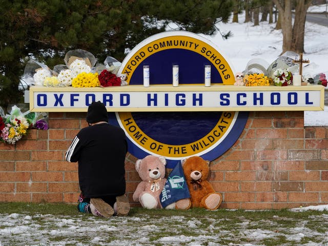 Un bienqueriente se arrodilla para orar en un monumento en el letrero de Oxford High School en Oxford, Michigan