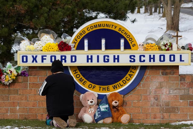 <p>A well wisher kneels to pray at a memorial on the sign of Oxford High School in Oxford, Michigan</p>
