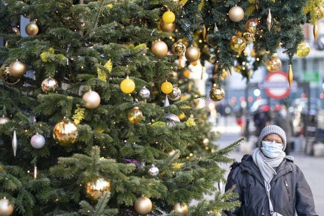 A woman wears a mask as she walks past Christmas decorations in London’s Knightsbridge (Dominic Lipinski/PA)