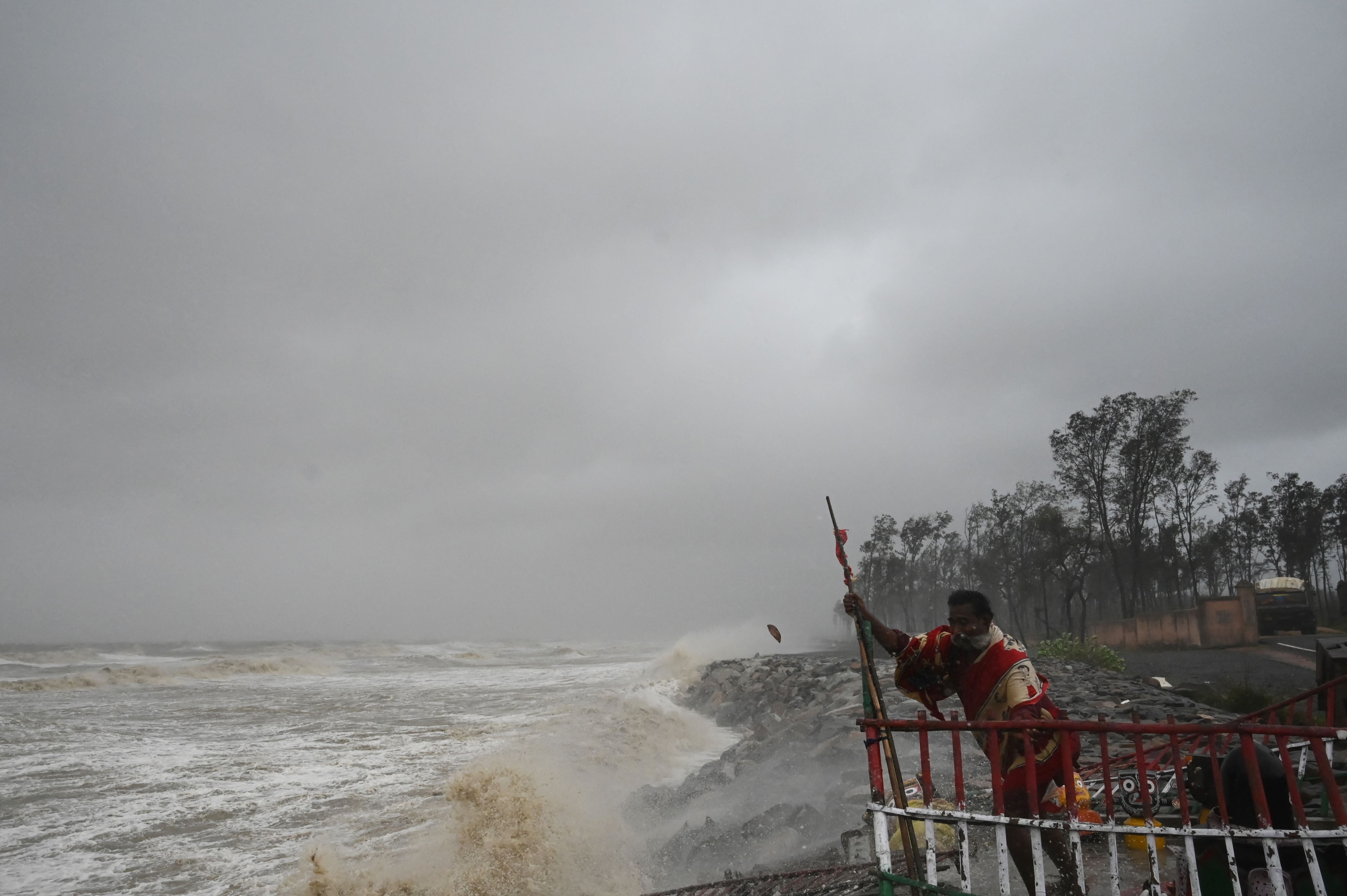A Hindu priest holds onto a fence at a seafront temple while strong winds batter Balasore district in Odisha
