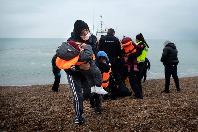 <p>A woman carries her children after being helped ashore from a RNLI lifeboat at a beach in Dungeness</p>