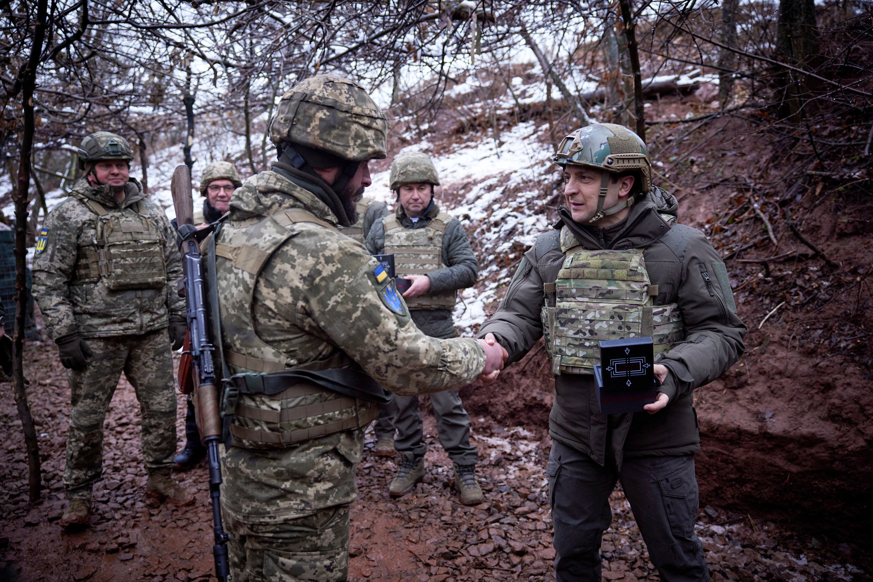 Ukrainian President Volodymyr Zelenskyy, right, awards a soldier in a trench as he visits the war-hit Donetsk region, eastern Ukraine, Monday, Dec. 6, 2021. (Ukrainian Presidential Press Office via AP)