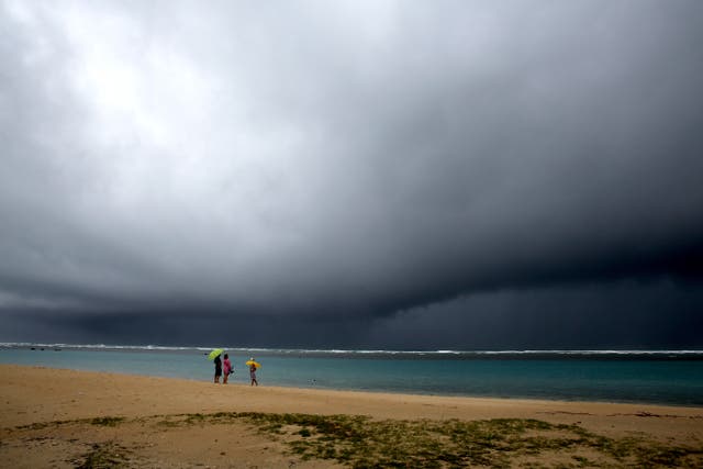 <p>People hold umbrellas as rain falls on an otherwise empty beach in Honolulu on Monday. A strong storm packing high winds and extremely heavy rain flooded roads and downed power lines and tree branches across Hawaii</p>