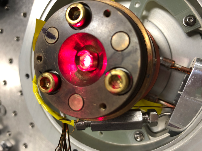 A strong laser is seen illuminating a material in a low-temperature chamber. The laser is being used to change the material's degree of transparency