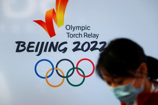 <p>A woman wearing a face mask stands in front of the logo of the Beijing 2022 Winter Olympics before the Olympics flame exhibition tour at Beijing University of Posts and Telecommunications, in Beijing, China on 9 December 2021</p>