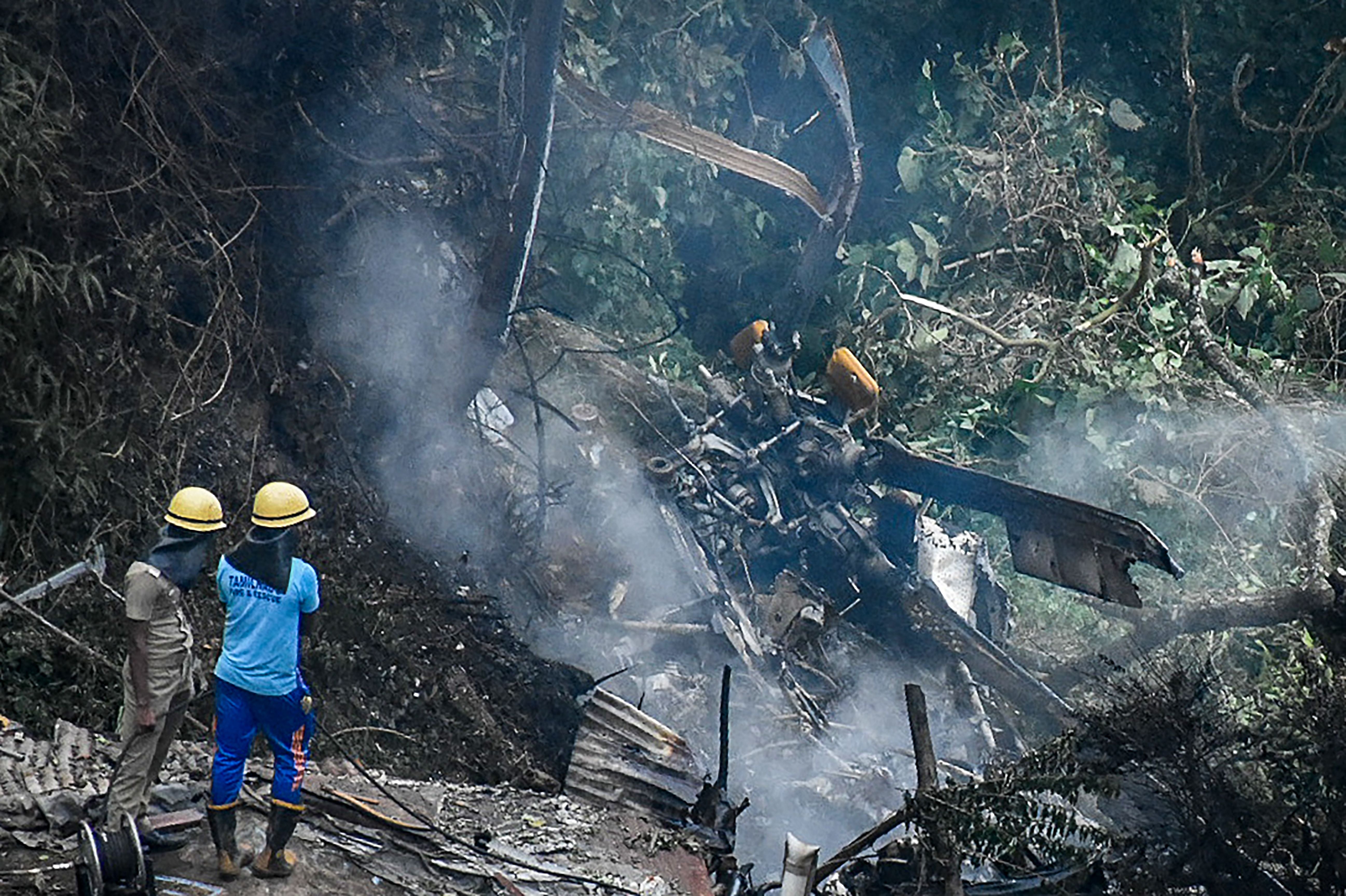 Firemen and rescue workers stand next to the debris of an IAF Mi-17V5 helicopter crash site