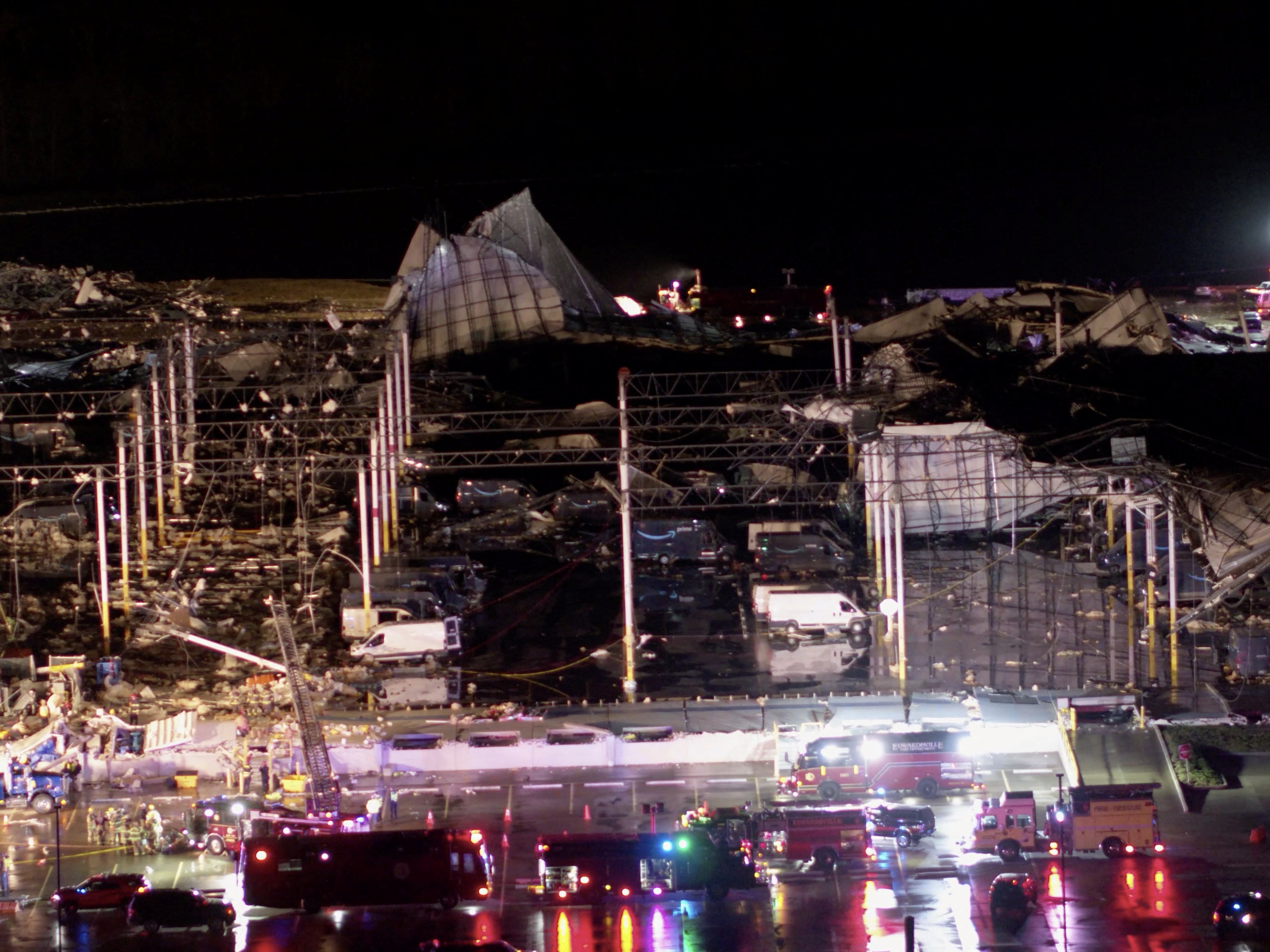 Delivery vehicles with the Amazon Prime logo sit parked at a damaged Amazon.com, Inc warehouse as emergency crews respond after a tornado passed through Edwardsville, Illinois, U.S., December 10, 2021