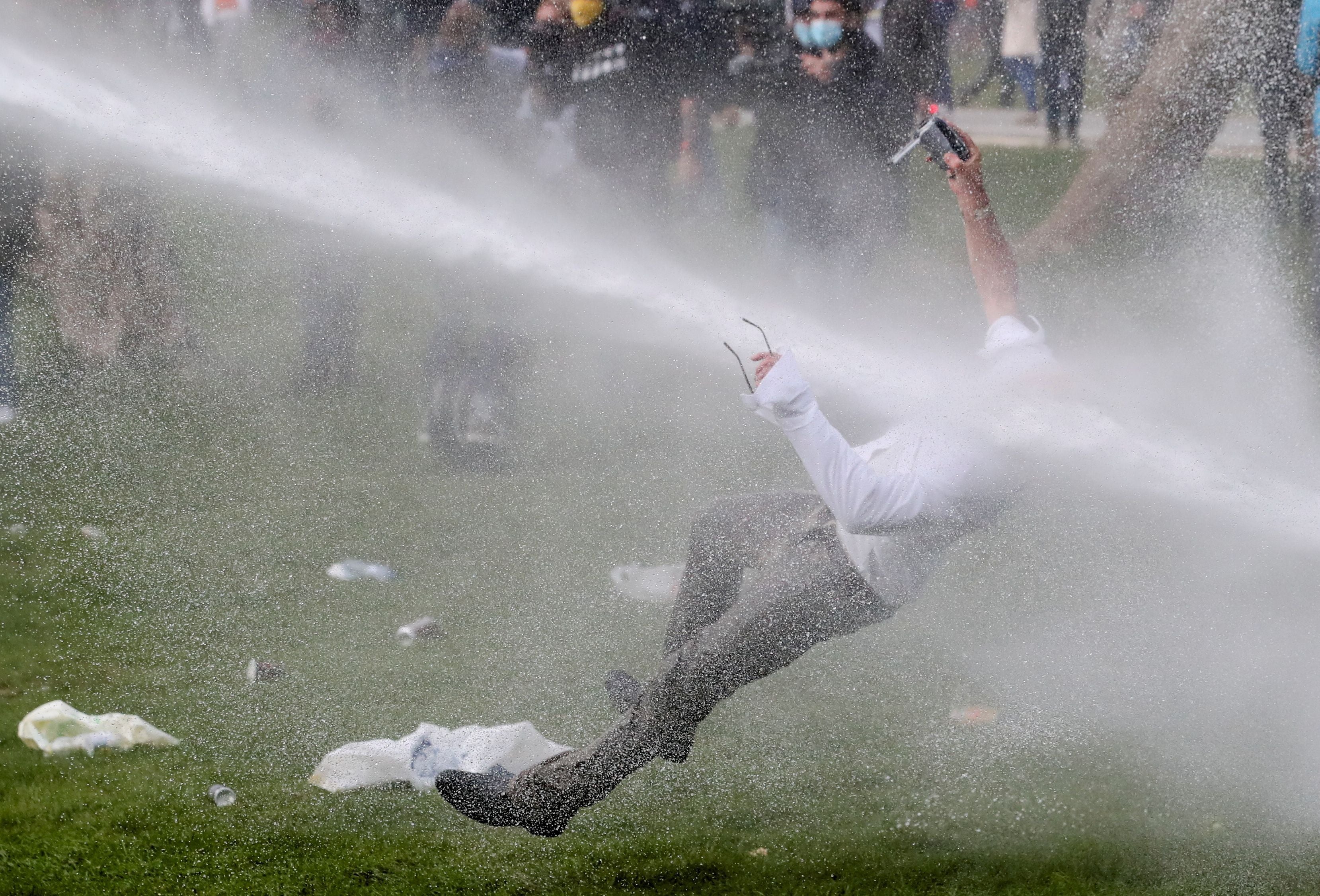 A man is knocked over by a water cannon during clashes as people gather in a park in defiance of Belgium’s Covid restrictions in Brussels