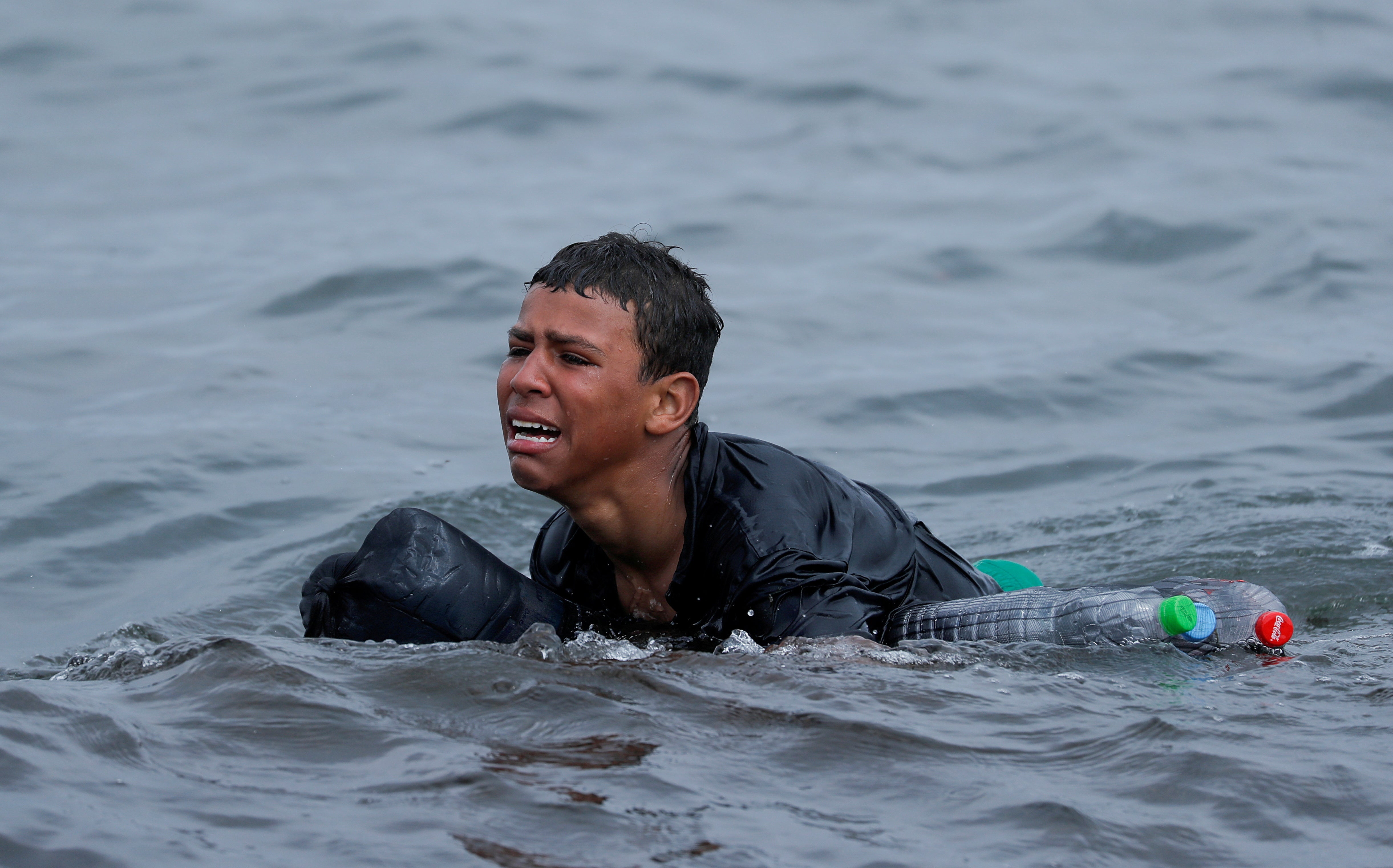 Achraf, 16, cries as he swims using bottles as floats near the fence between the Spanish-Moroccan border, after thousands of migrants swam to Ceuta, Spain, from Morocco
