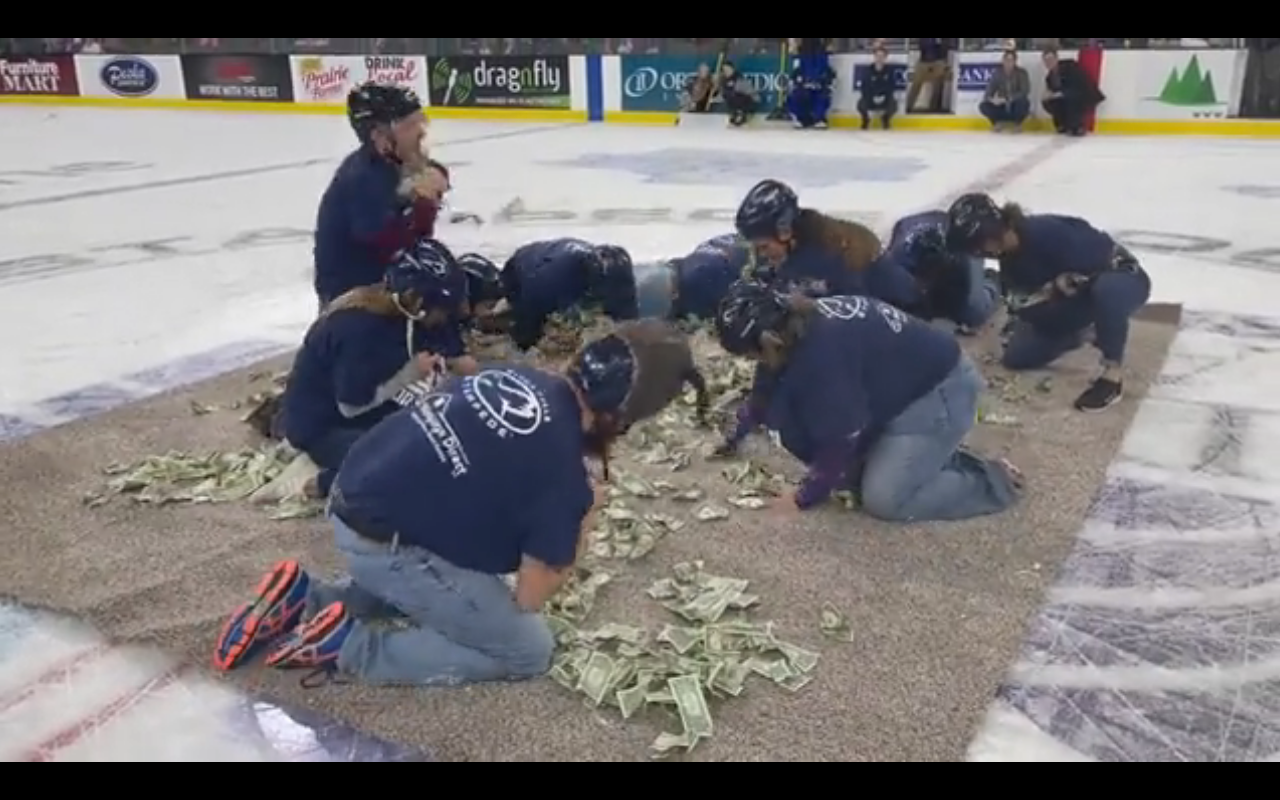 Ten teachers are seen here collecting dollar bills off a mat in the middle of a hockey stadium