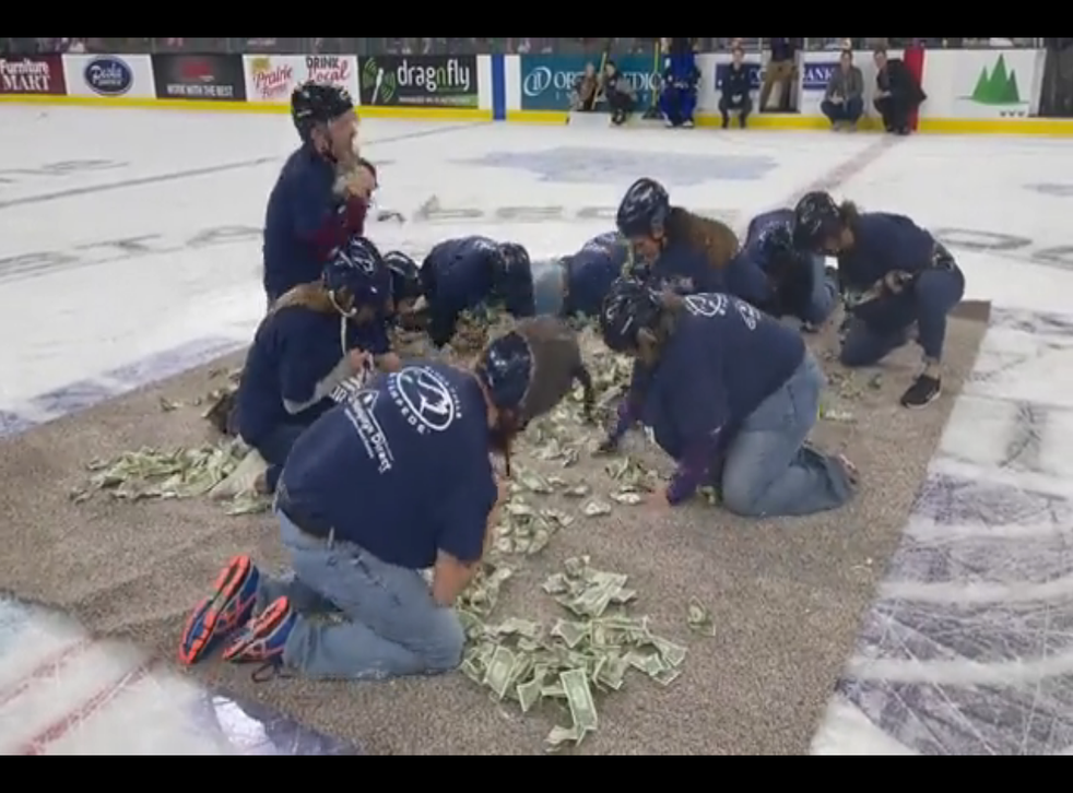<p>Ten teachers are seen here collecting dollar bills off a mat in the middle of a hockey stadium</p>